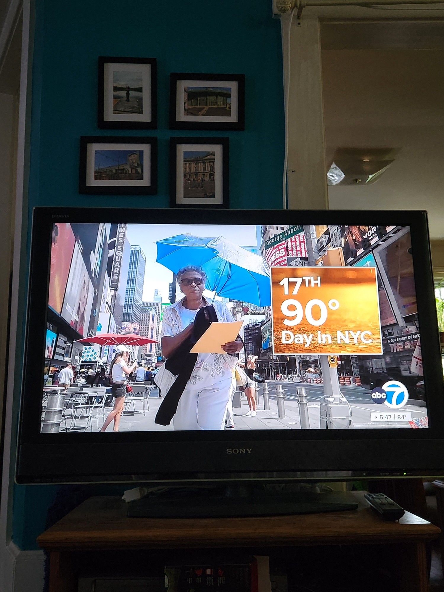 A woman walking down the street using an umbrella to shield herself from the song. Next to her is a graphic reading "17th 90 degree day in NYC"