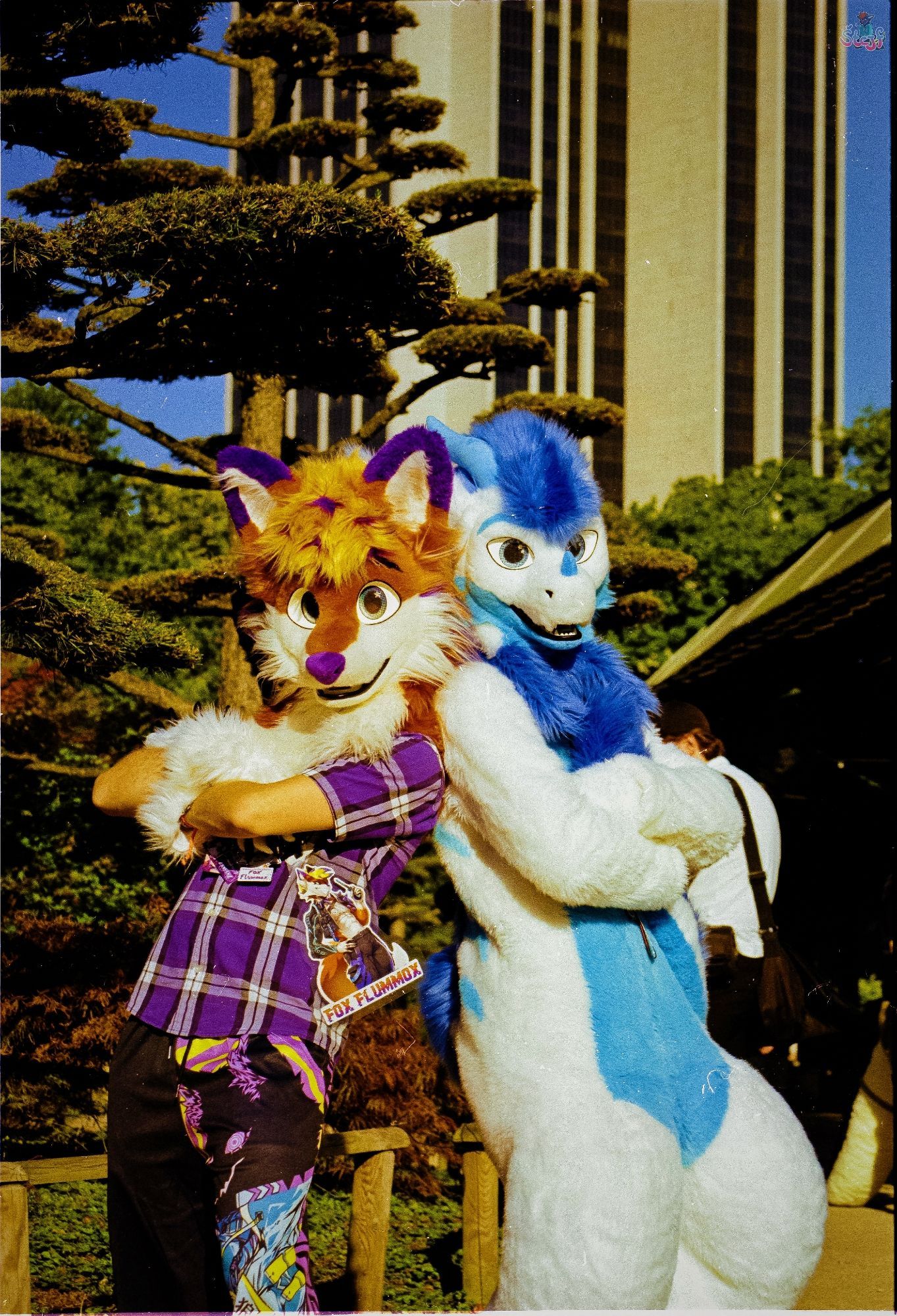 Two suiters, Fraxinas on the left and Reiko on the right standing back to back in sunny Planten un Blomen with the tower of the Radisson hotel in Hamburg visible in the background.