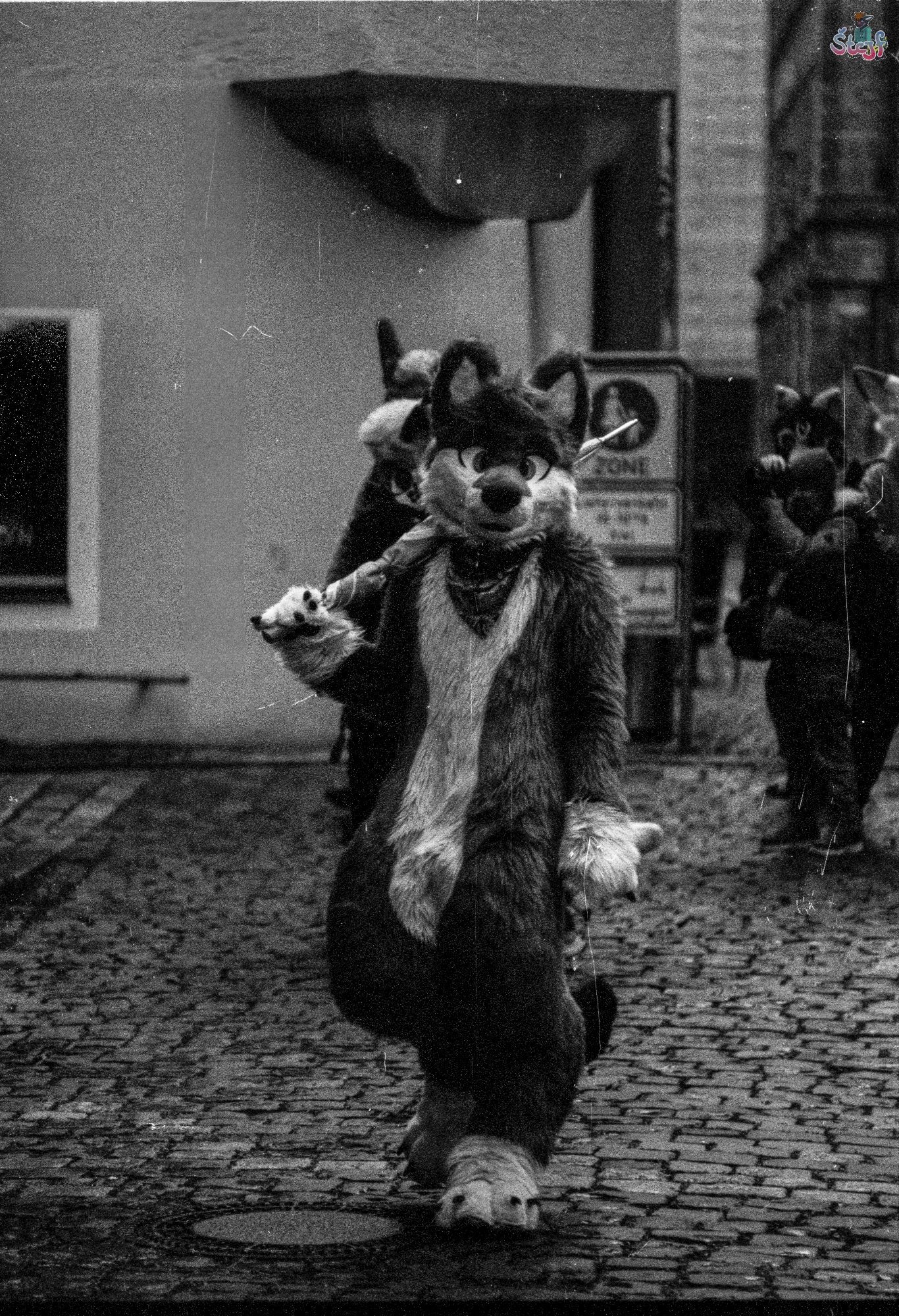 A suiter on a street corner with a closed umbrella over his right shoulder.