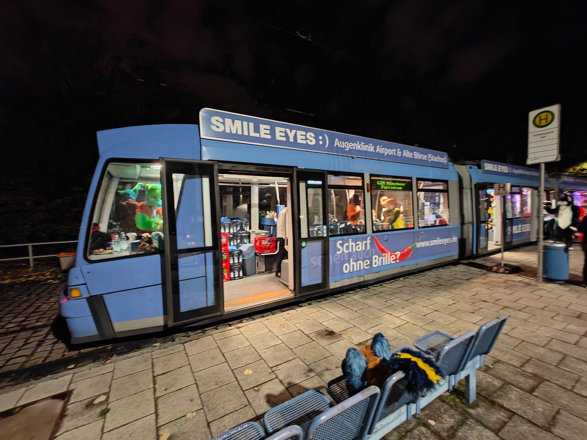 Picture of the rear of a tram commonly used in Munich. It's parked at a platform with doors open. Inside are some Fursuiters getting ready for the imminent departure.