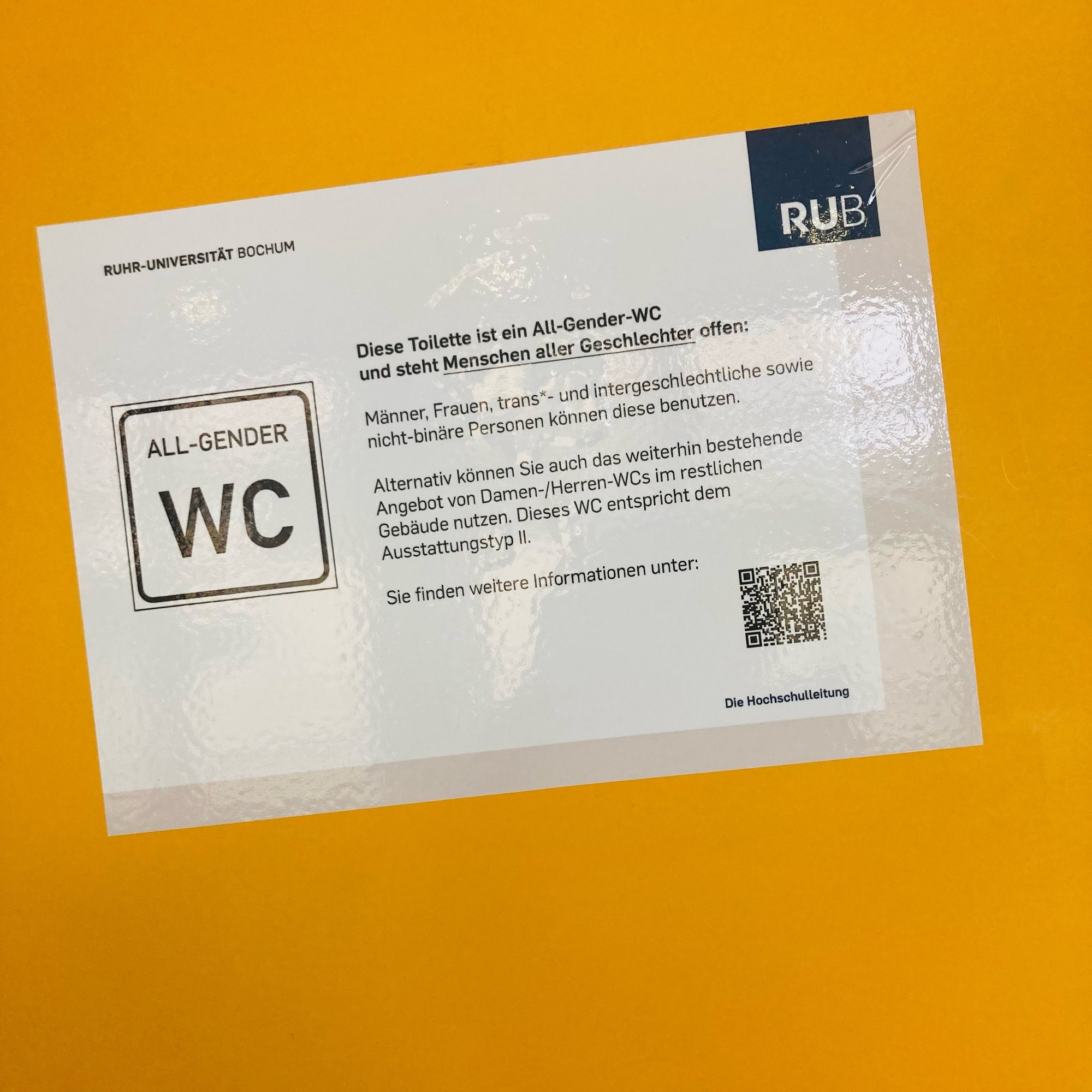 foto eines schildes an einer tür: 
RUB, ALL-GENDER WC. Diese Toilette ist ein All-Gender-WC und steht Menschen aller Geschlechter offen: Männer, Frauen, trans*- und intergeschlechtliche sowie nicht-binäre Personen können diese benutzen. Alternativ können Sie auch das weiterhin bestehende Angebot von Damen-/Herren-WCs im restlichen Gebäude nutzen. Dieses WC entspricht dem Ausstattungstyp II.
Sie finden weitere Informationen unter: qr-code.