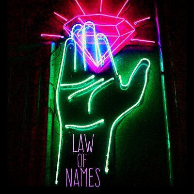 A neon sign of a green hand, palm toward the camera, holding a neon pink diamond. The words Law of Names are printed in lighter pink in the wrist of the hand