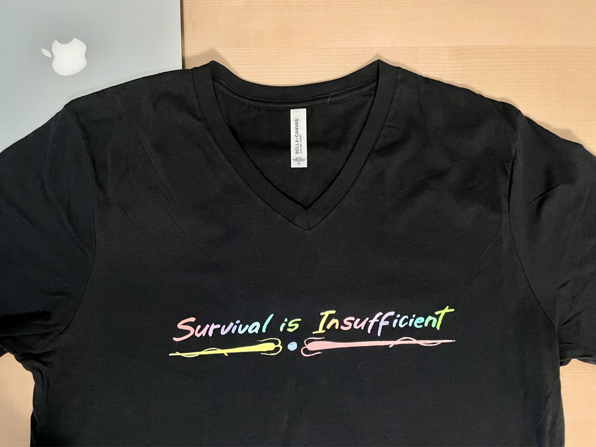 Black v-neck t-shirt with a multi-color rendition of the “Survival is Insufficient” artwork as seen on the side window of a vehicle in Station Eleven.