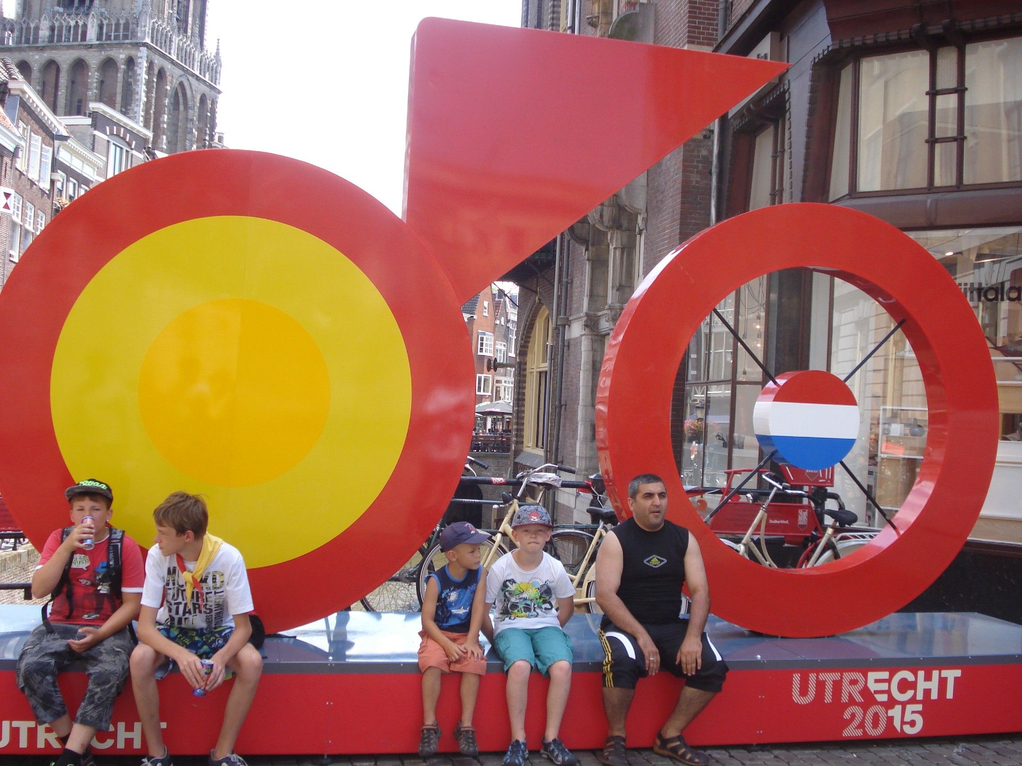 In Utrecht city center a large sculpture of a bike. It is bright red, and the front wheel is filled in with bright yellow, the body of it is a red triangle and the back wheel has spokes but the middle a circle with the dutch flag colours (red white and blue). 5 people are sitting along it, two of which are my children. it says on it, Utrecht 2015.