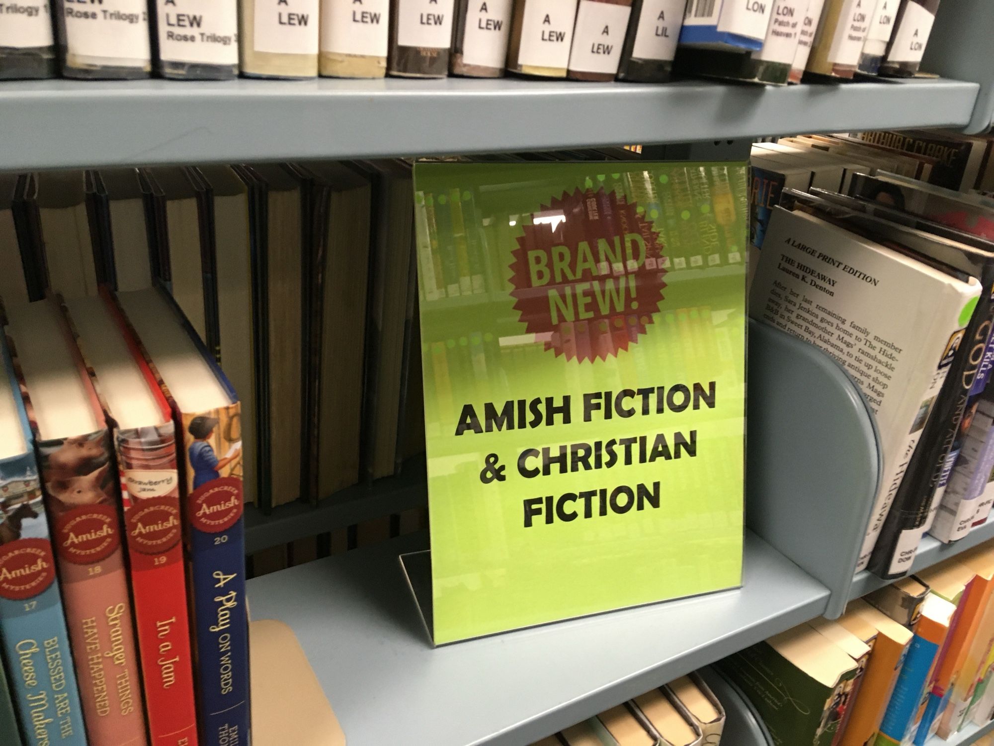 Sign on a library bookshelf reads “brand new Amish Christian and fiction”