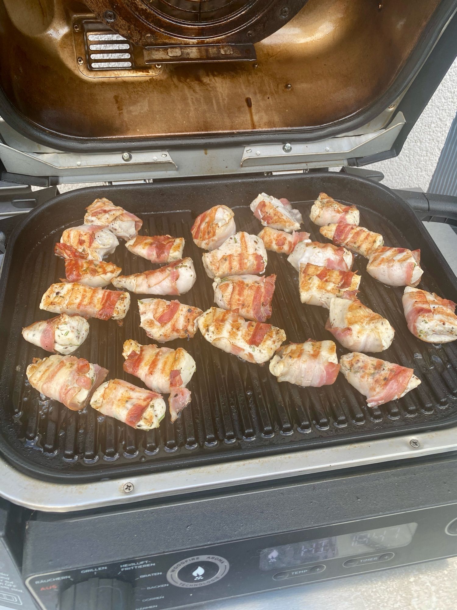 Stückchen von der Hühnerbrust im Speckmantel auf einem Grill mit offenem Deckel