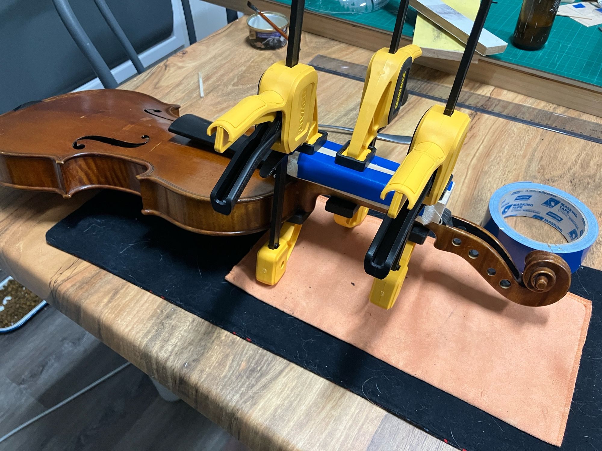 A violin on a workbench, with clamps holding on a freshly glued fingerboard.