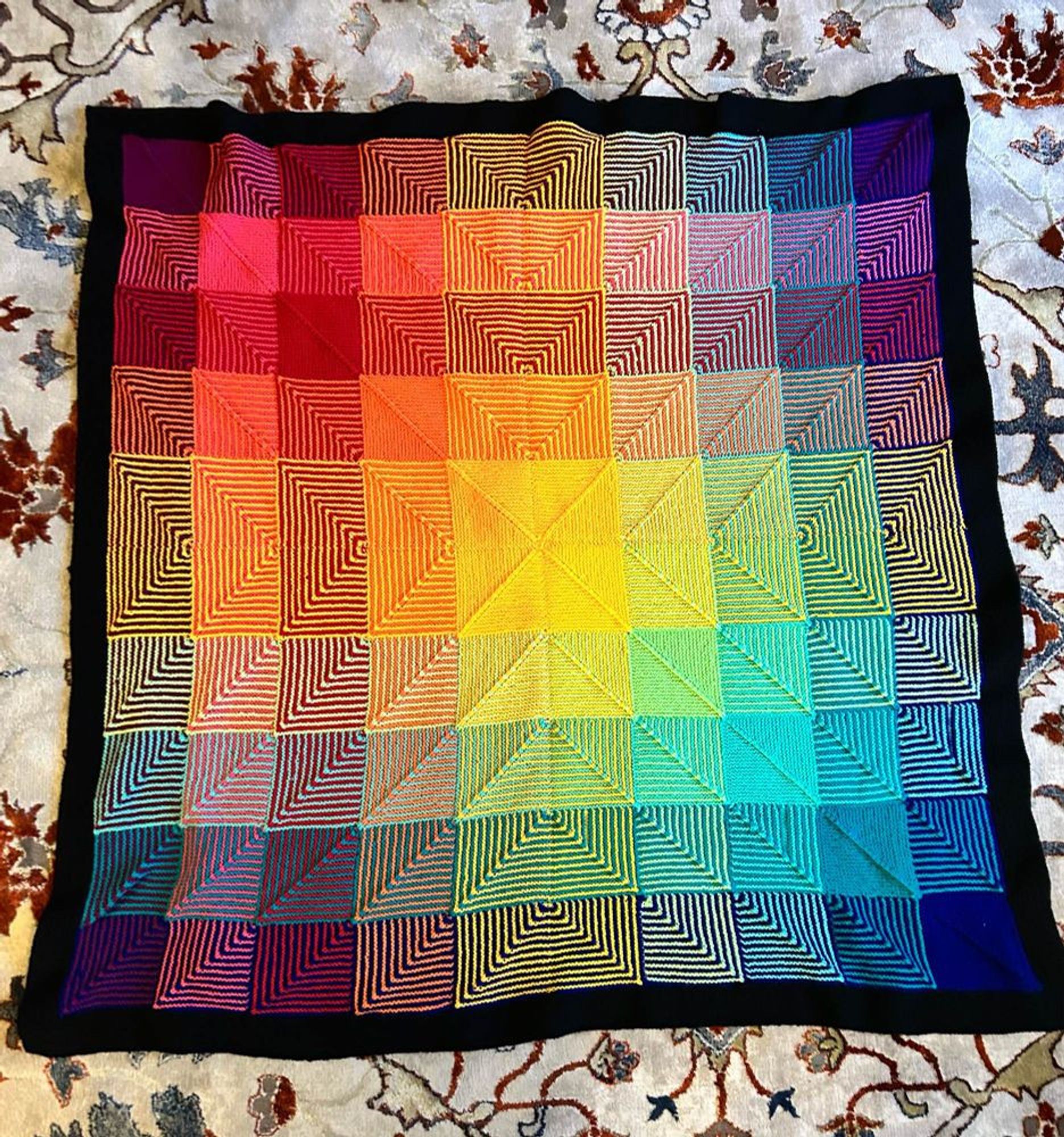 a colorful afghan spread out on the floor. The afghan is made of rainbow colored knitted squares