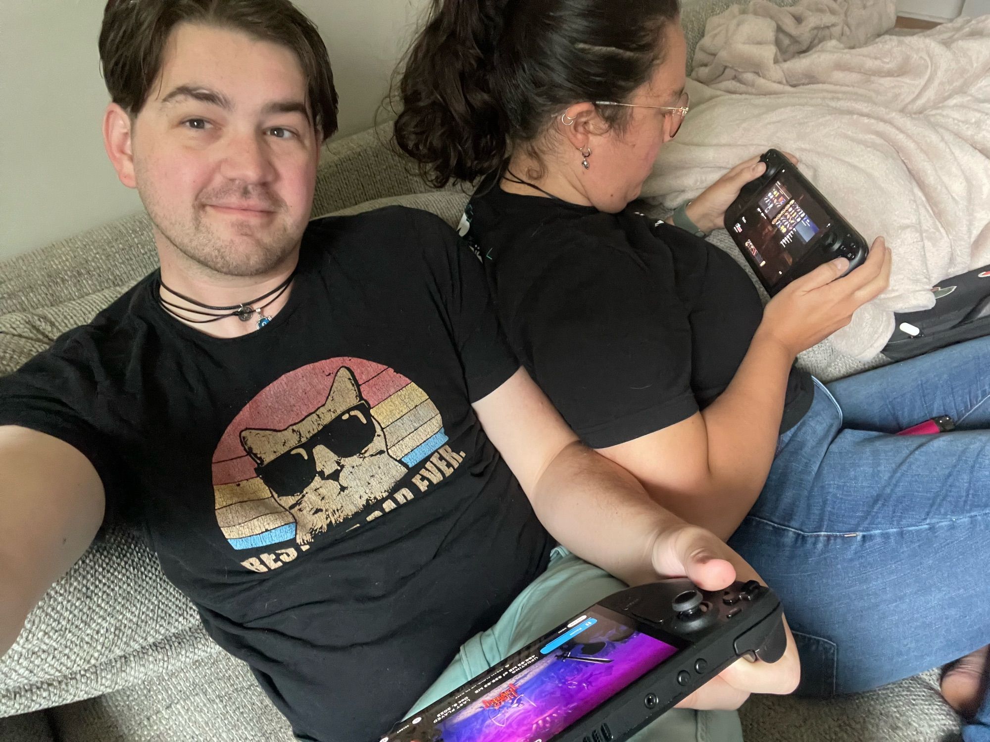 A photo of me and my girlfriend, sitting back to back, both playing Steam Decks. She is playing return to Moria and I am playing halls of torment.