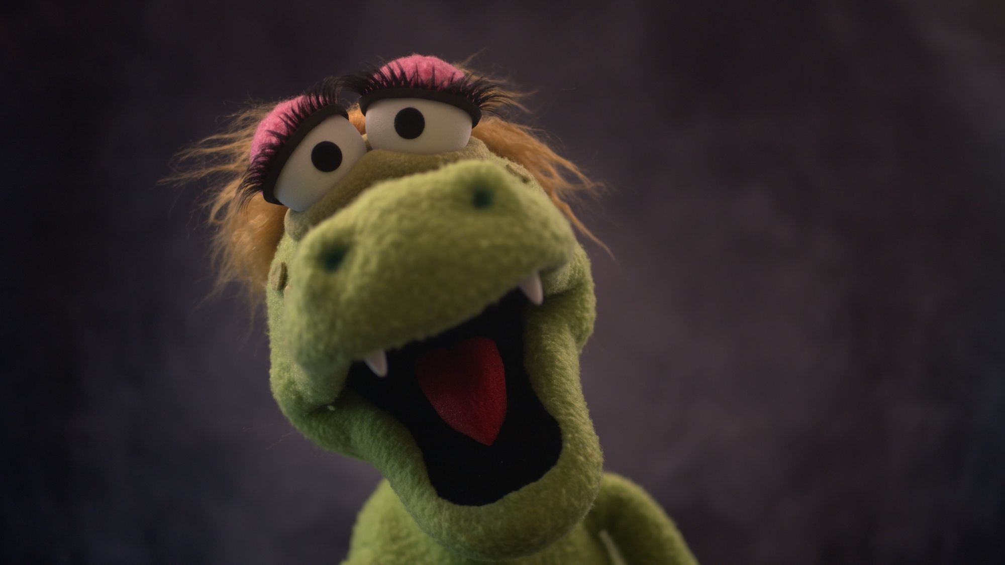 Closeup view of a green alligator puppet with blonde hair and large eyelashes