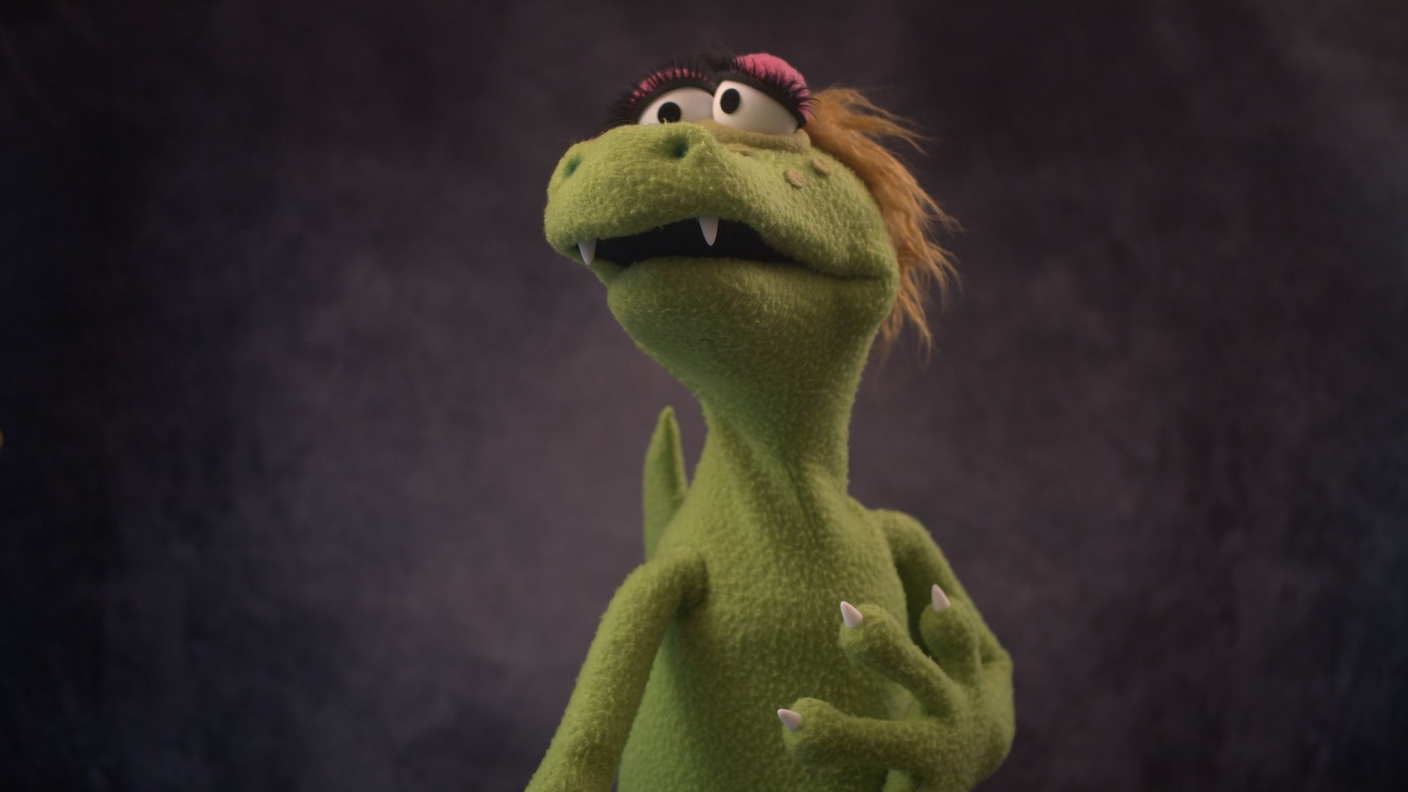 Left view of a green alligator puppet with blonde hair and large eyelashes