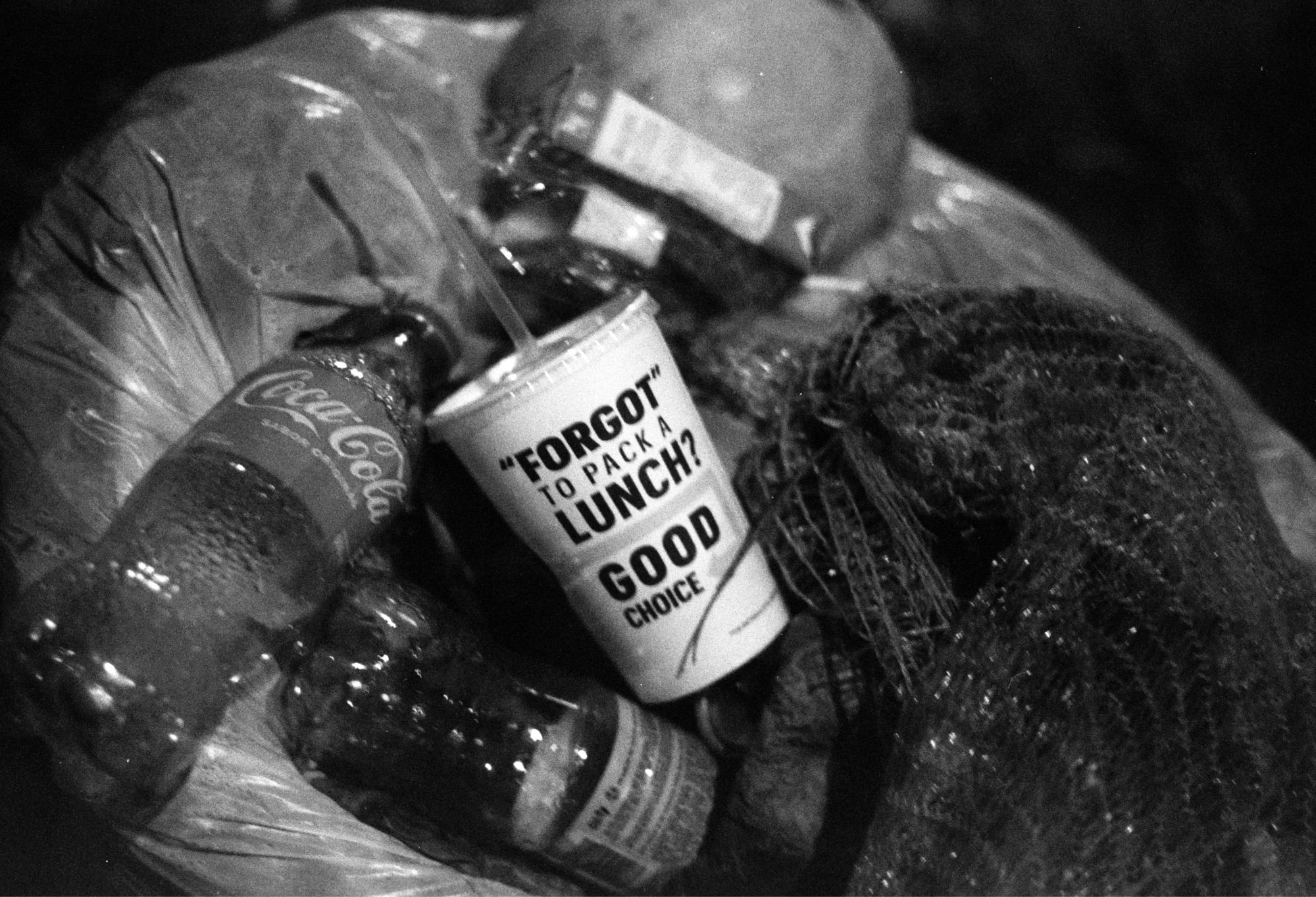 a black and white photograph shot on 35mm film of some garbage where there’s a carton vase in the center that reads “forgot to pack a lunch? good choice”