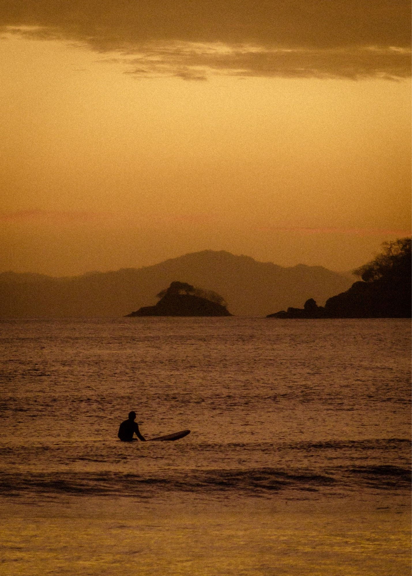 image of a man on a surfboard waiting for a wave at sunset. 