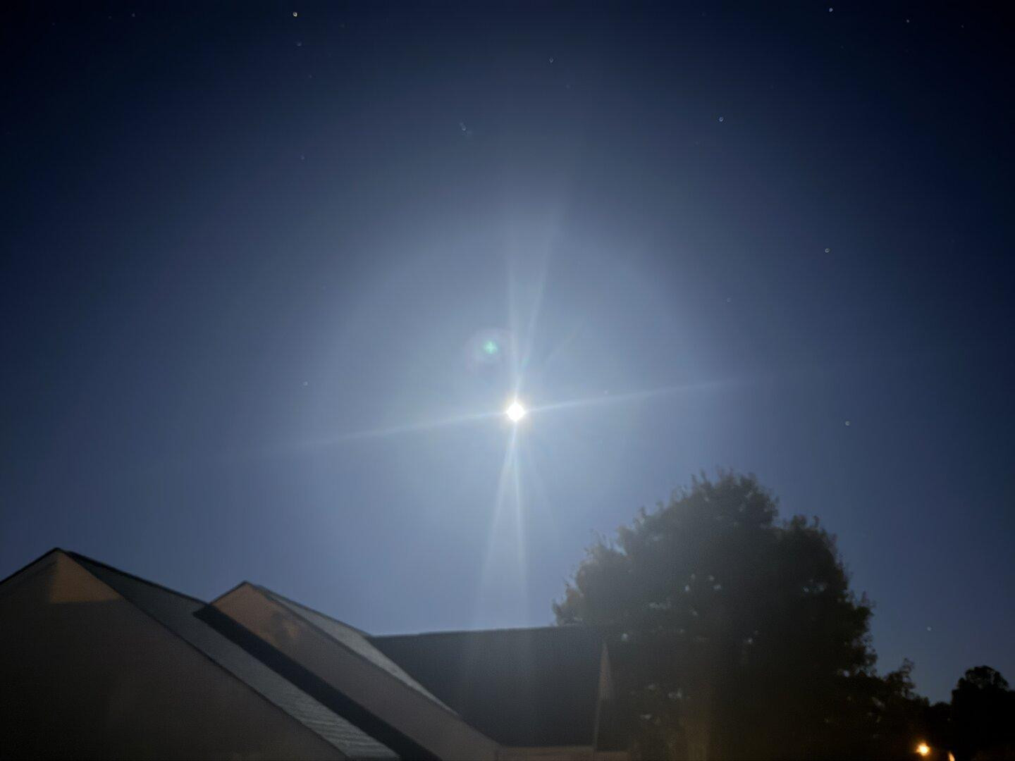 A photo of the moon at around 5:30am EST. You can see the moon itself, though it's blurry, some of the other stars around it, the night sky, part of the neighbors house.