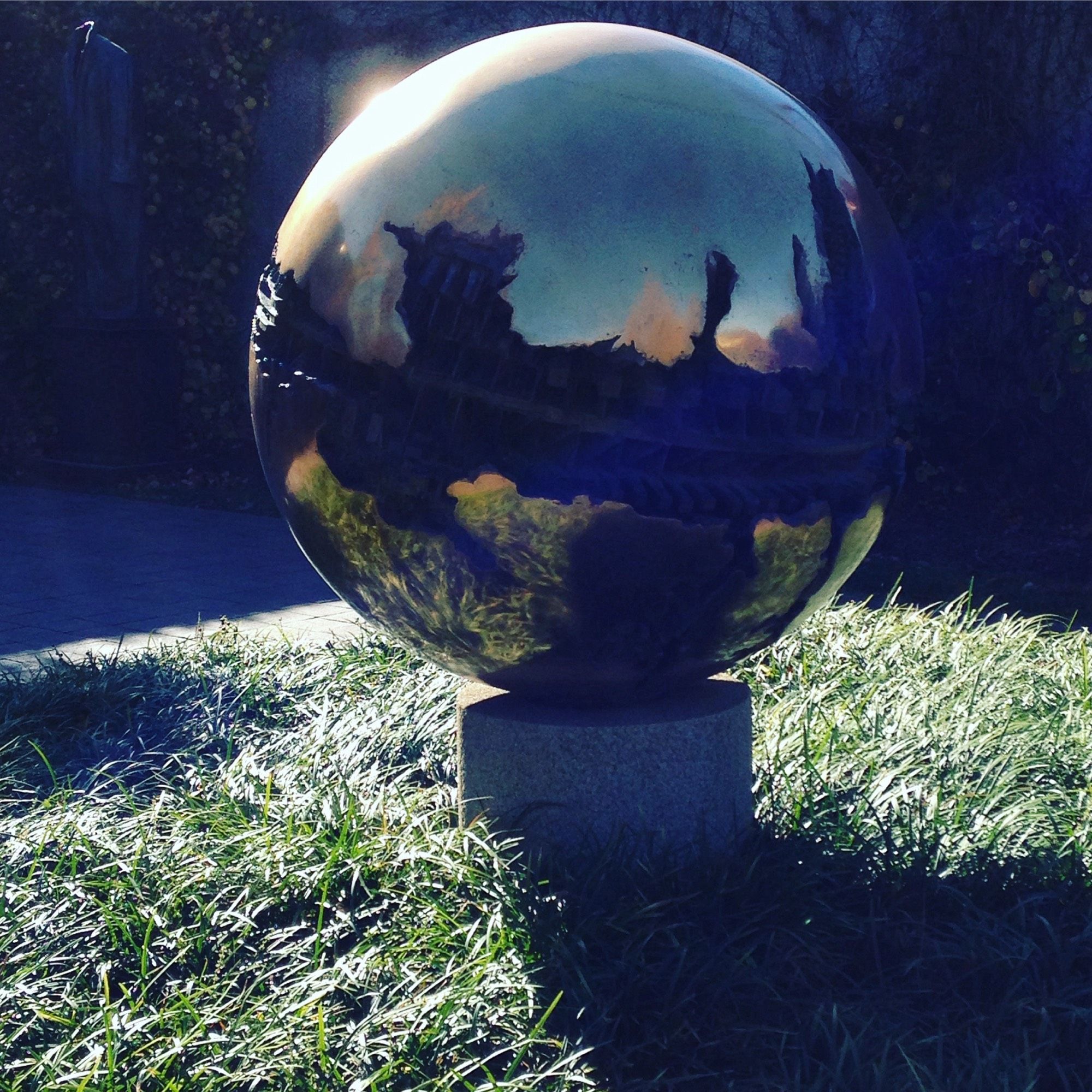 SPHERE NO. 6 (SPHERE WITHIN A SPHERE) - A shiny metallic spherical object reflects the sky and the Smithsonian in its surface like mirror on a bright sunny day. The sculpture is made of bronze and is roughly 45” X 46” X 47” in size. Up close, you can see that the surface of the sphere is deeply carved, like our globe by glaciers, all around its ‘equator’; on the back side, it’s interior is exposed as if it contained an alien form inside. The whole sphere rests on a stone-cube pedestal on grass in the Sculpture Garden at the Hirshhorn Museum, Washington, DC (November 2015).
Note: The Sculpture Garden has since gone through a big renovation; I’m not sure if its collection will have changed or remain the same when it reopens later this year (September 2024).