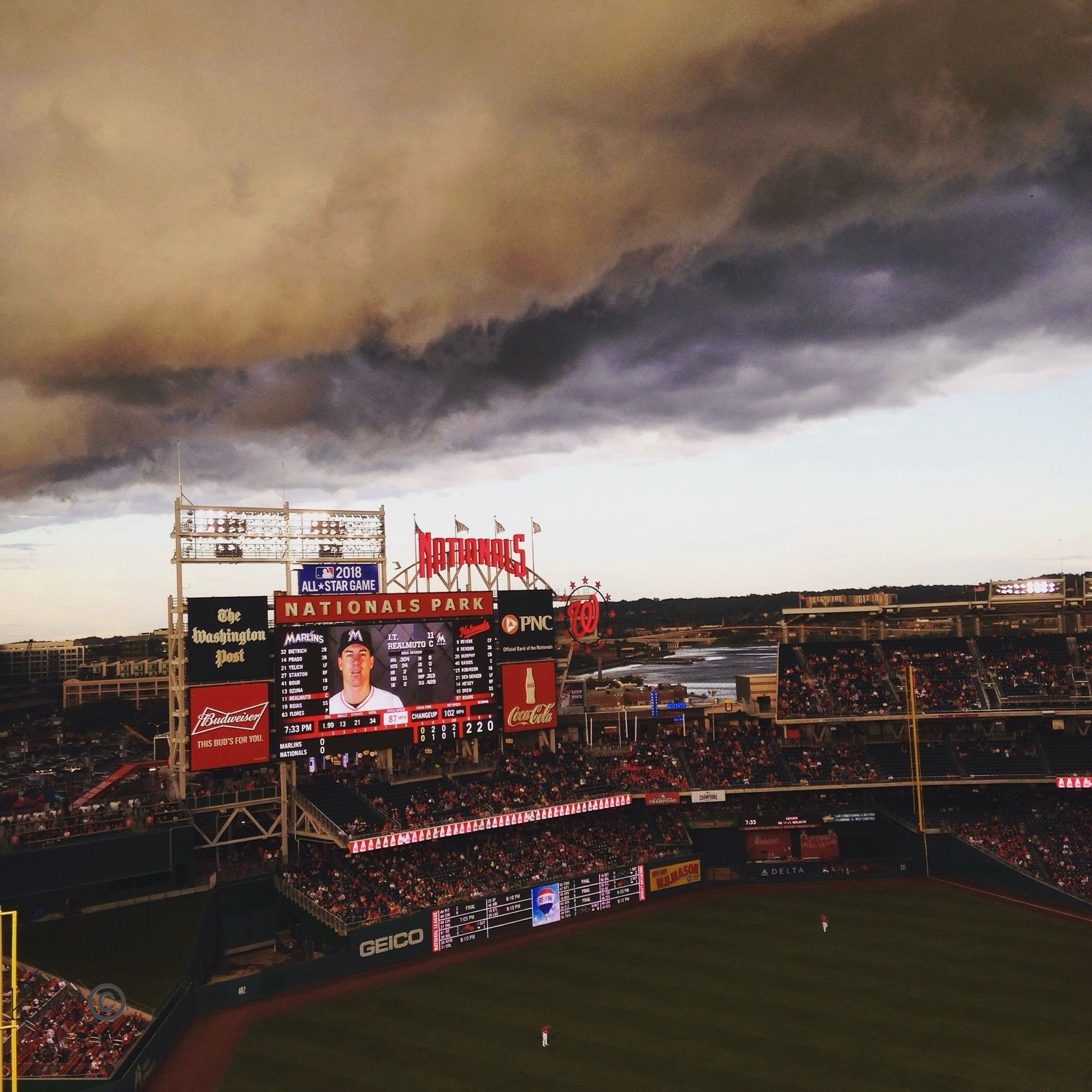 View from the upper deck of Nationals Park with the baseball game still being played under stadium lights as a dark thundercloud hovers over the ballpark like a gigantic spaceship. The sky is otherwise clear on a cool spring day in May (2016).