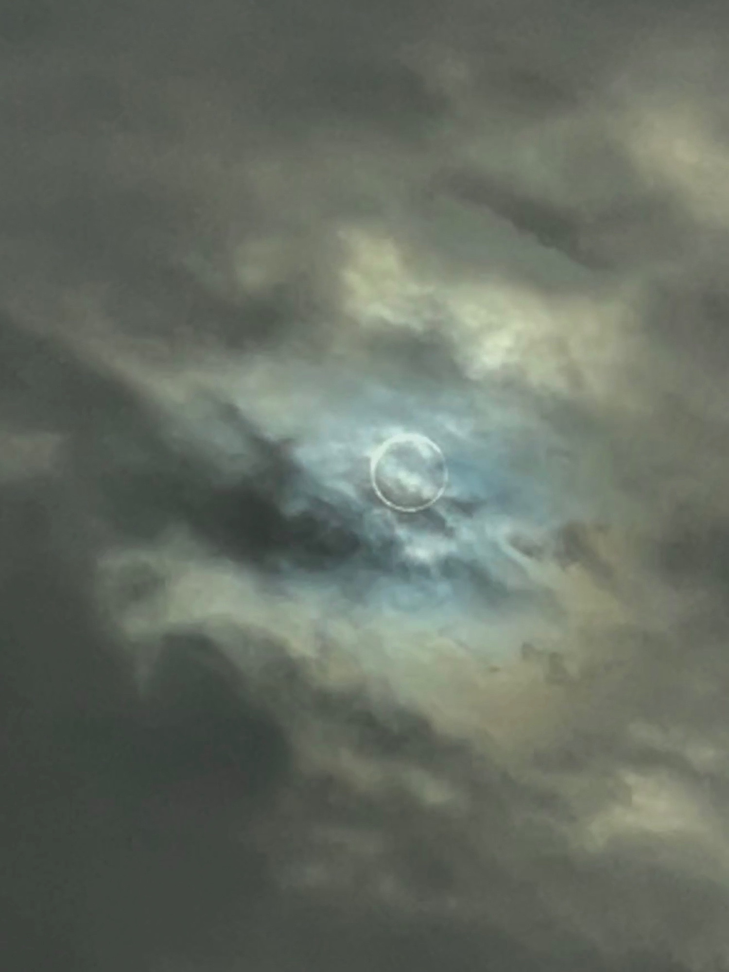 Clouds with a bright ring of white. The moon almost covering the sun.