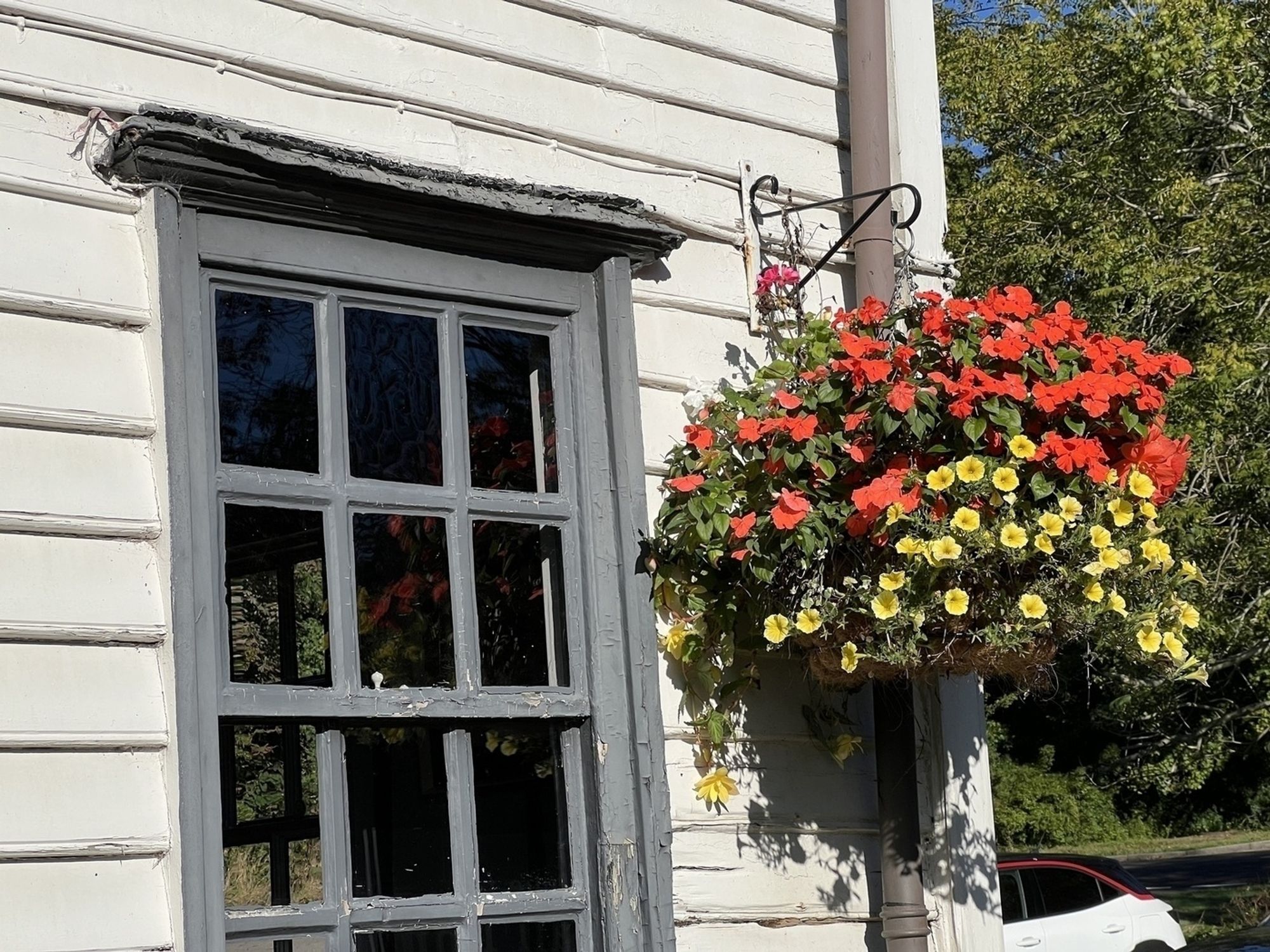 A weathered wooden window beside a colorful hanging basket filled with red and yellow flowers.