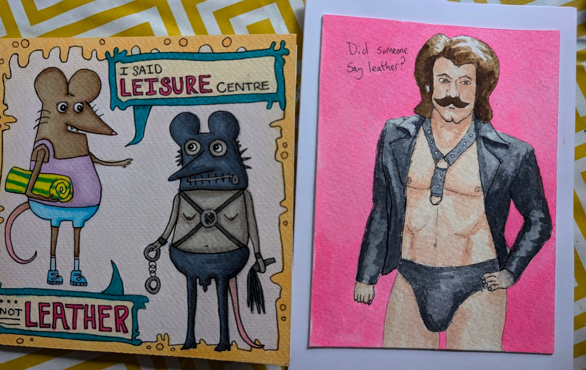 Two hand made cards. One is rats dressed in s&m leather, the other is a man with bouffant hair dressed in a leather posing pouch and harness. 