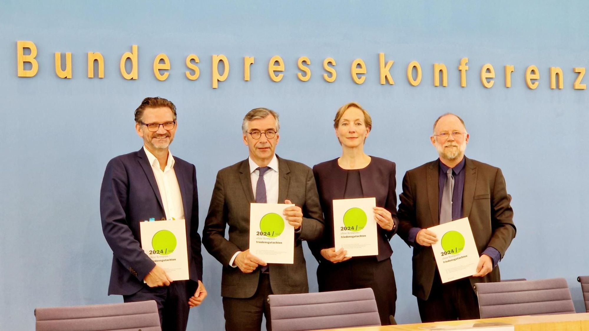 Eine Gruppe von vier Personen, hinter ihnen an einer Wand der Schriftzug Bundespressekonferenz. Sie halten alle eine Ausgabe des Friedensgutachtens in Händen. Zu sehen sind (v.l.): Prof. Dr. Conrad Schetter (BICC), Prof. Dr. Christopher Daase  (PRIF), Prof. Dr. Ursula Schröder (IFSH) und Prof. Dr. Tobias Debiel  (INEF/UDE).