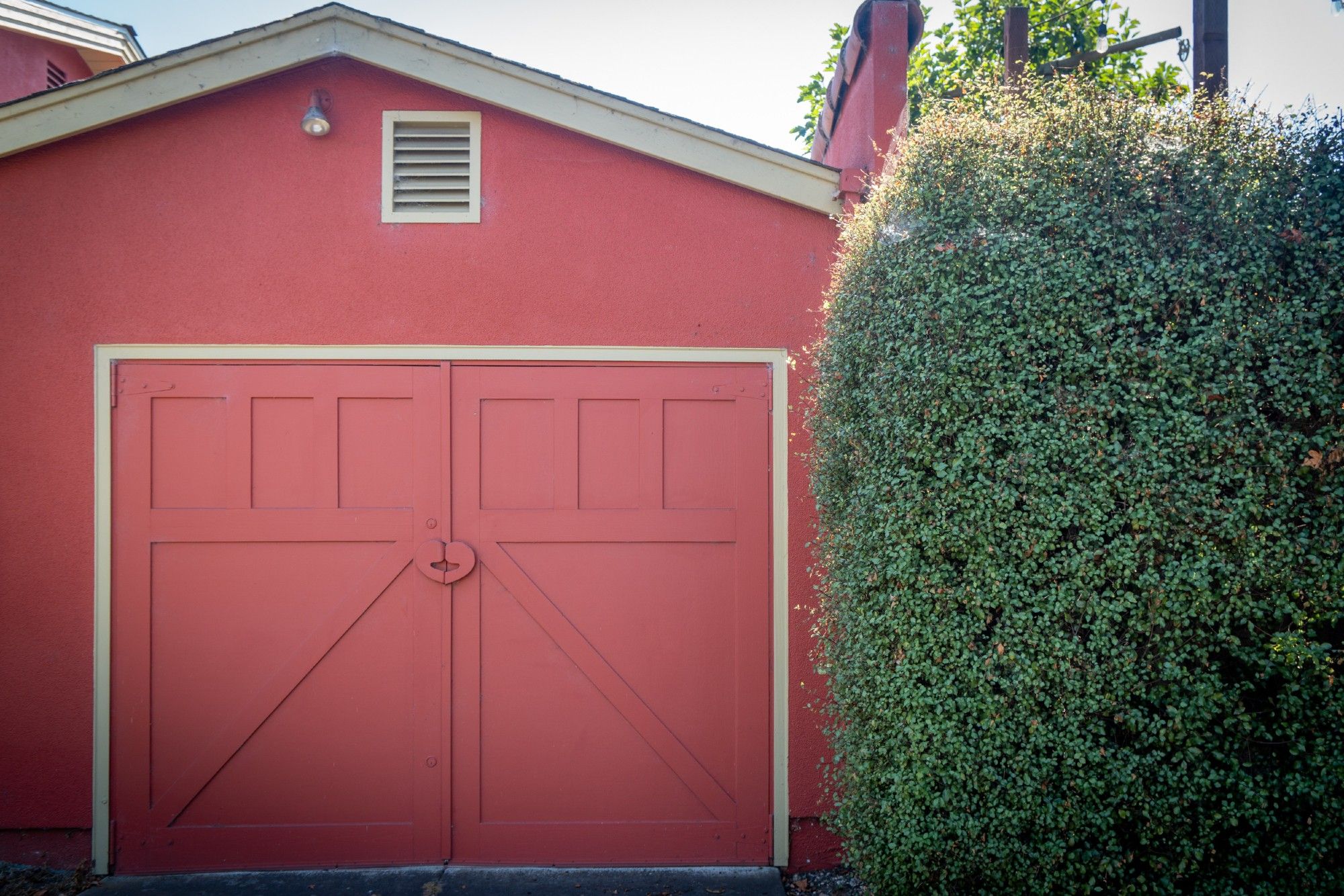 Red garage with door handle in the shape of a heart, next to green shrubbery