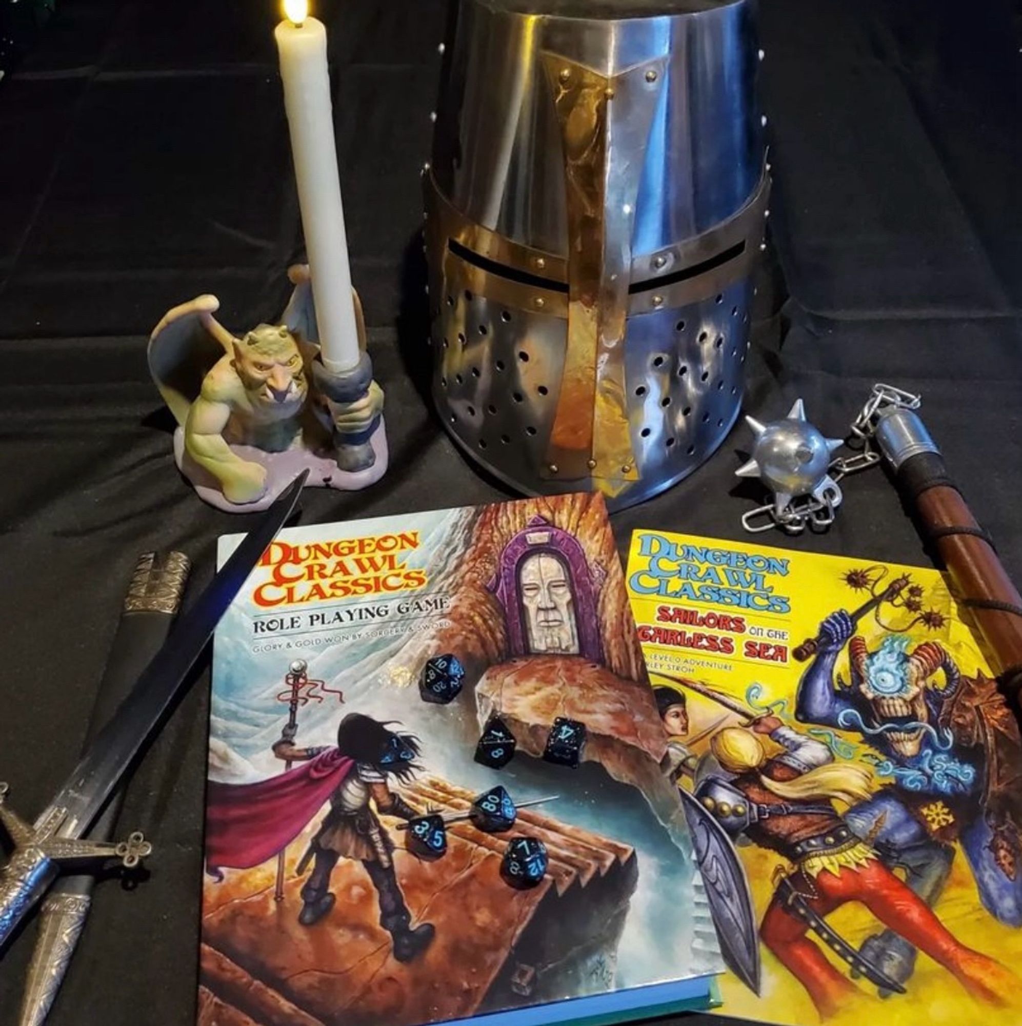 Dungeon Crawl Classics books with rpg dice and dungeon props of sword, helmet and mace