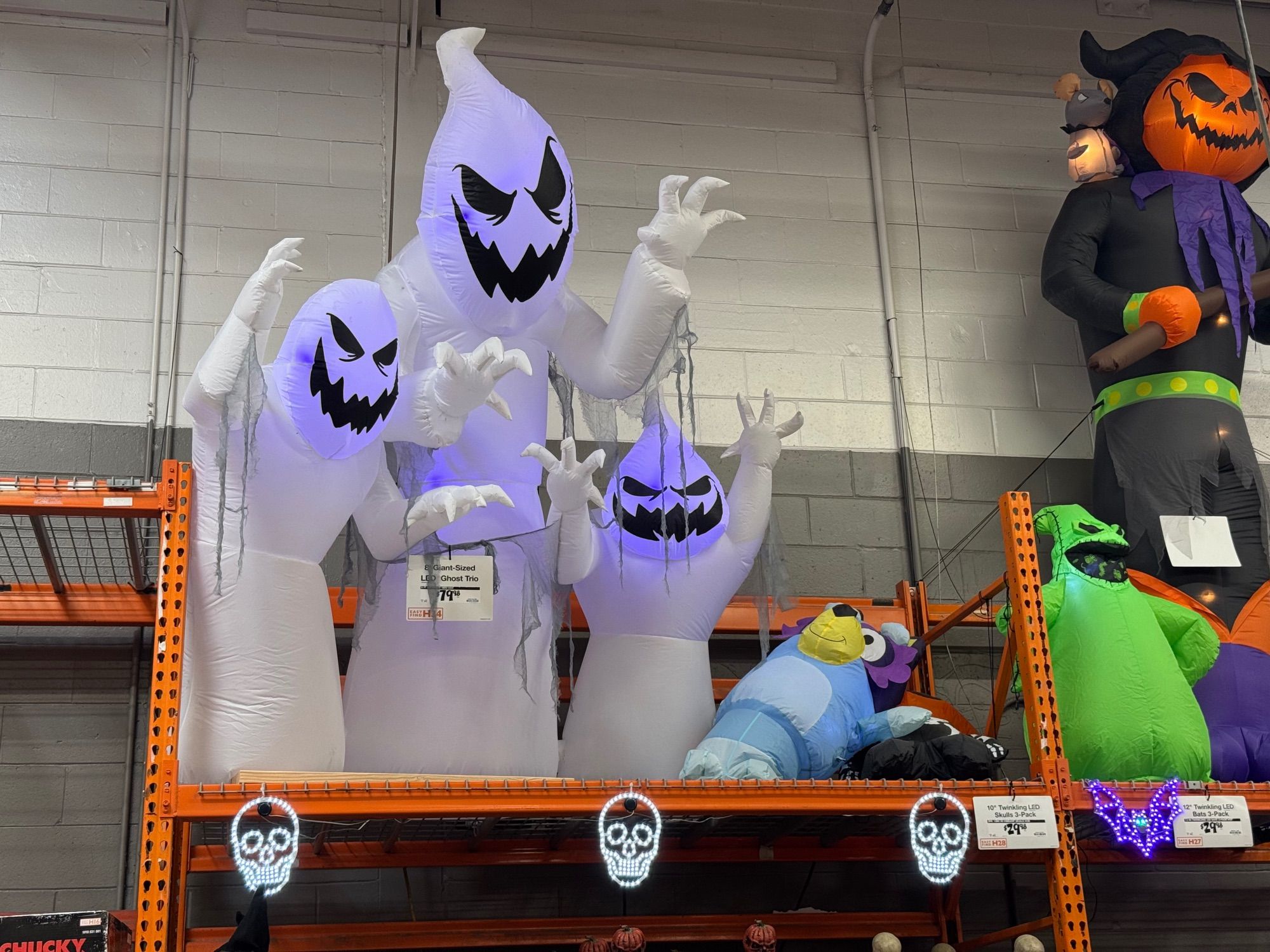 Inflatable decorative ghosts standing next to a knocked over inflatable decorative Bluey