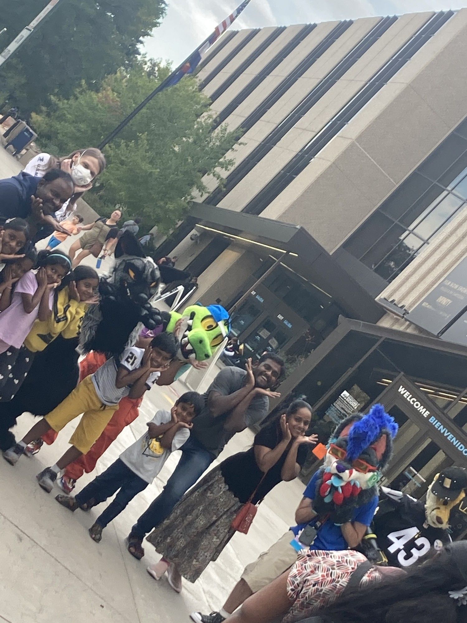 A photo of a bunch of varied fursuiters posing with families in front of the Denver Museum of Nature and Science.