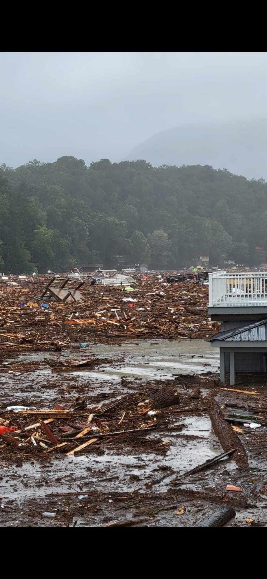 A flooded mountain landscape.  The floodwaters are filled with the rubble of houses.