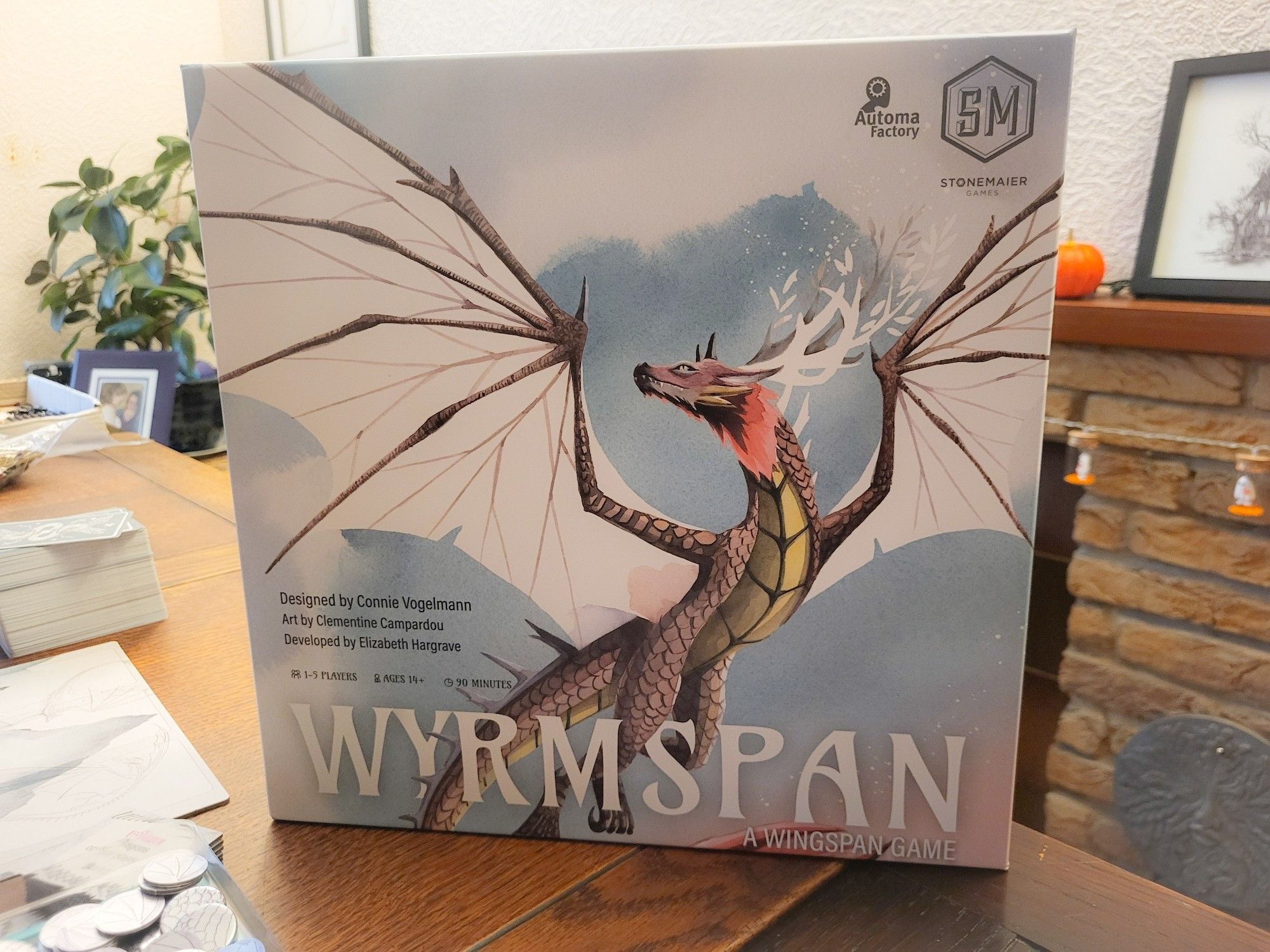 Board game box depicting a large brown and red dragon with large white wings outstretched against a blue sky with clouds