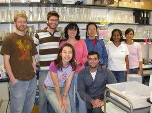 Eight people are smiling in a small laboratory.