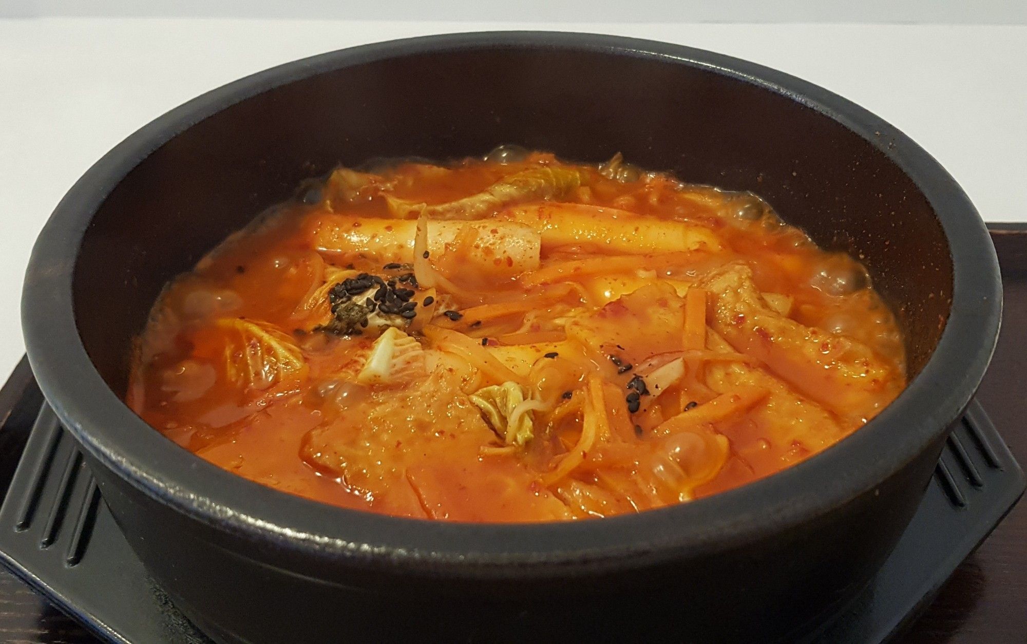 A pot of rice cakes, Korean fish cake, sweet potato noodles and random veg in a rich, orange coloured sauce which is literally boiling