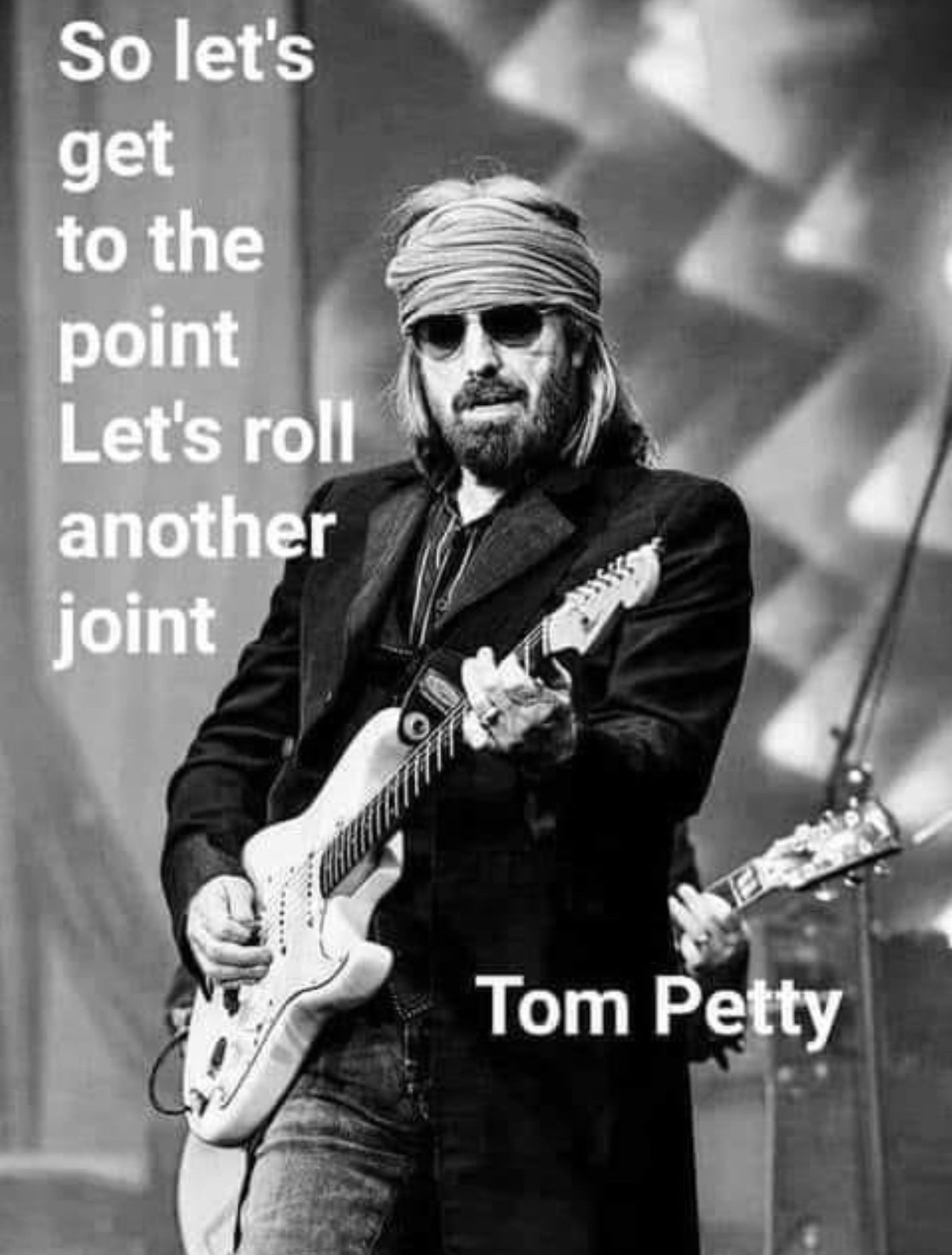 Black and white photo of Tom Petty holding his guitar.
“So let’s get to the point, let’s roll another joint.”