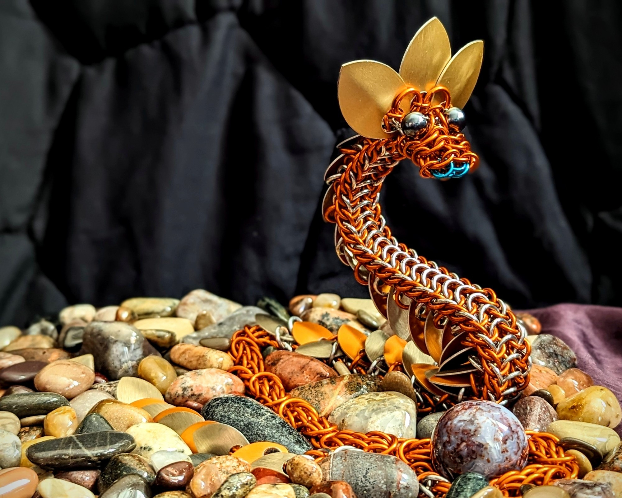 an orange dragon with gold fringe rests among it's collection of shiny stones