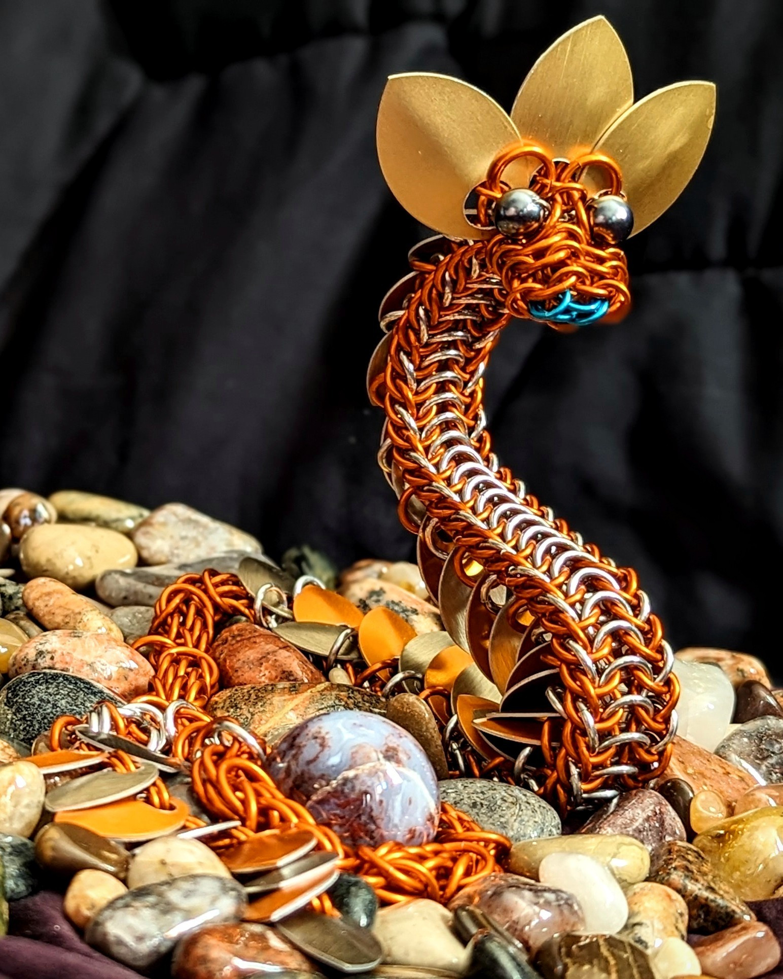 an orange dragon with gold fringe rests among it's collection of shiny stones