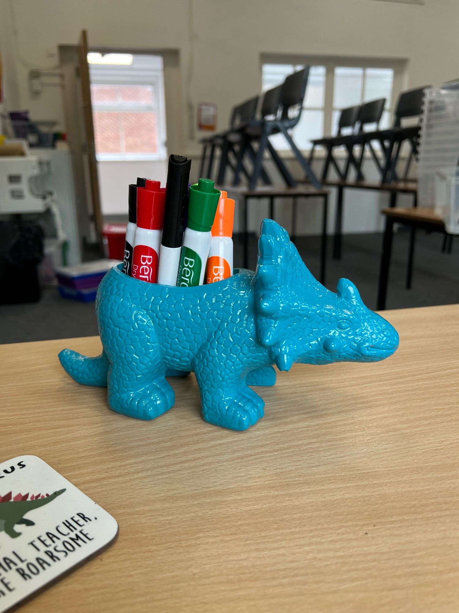 Blue Styracosaurus plant pot being used to hold whiteboard pens on a desk.