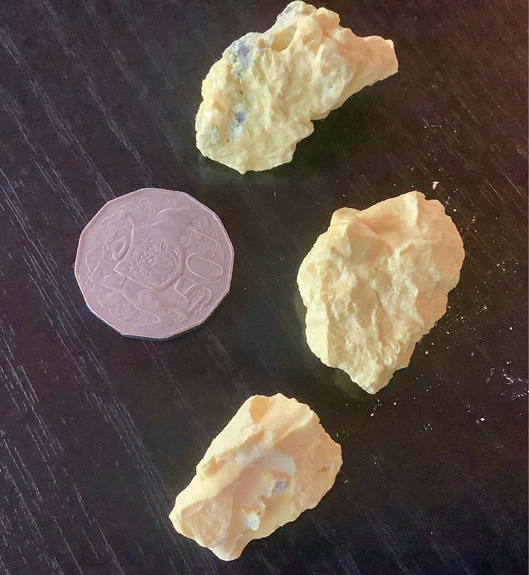 three yellow chunks of elemental sulphur on a black table, 50 cent piece for scale