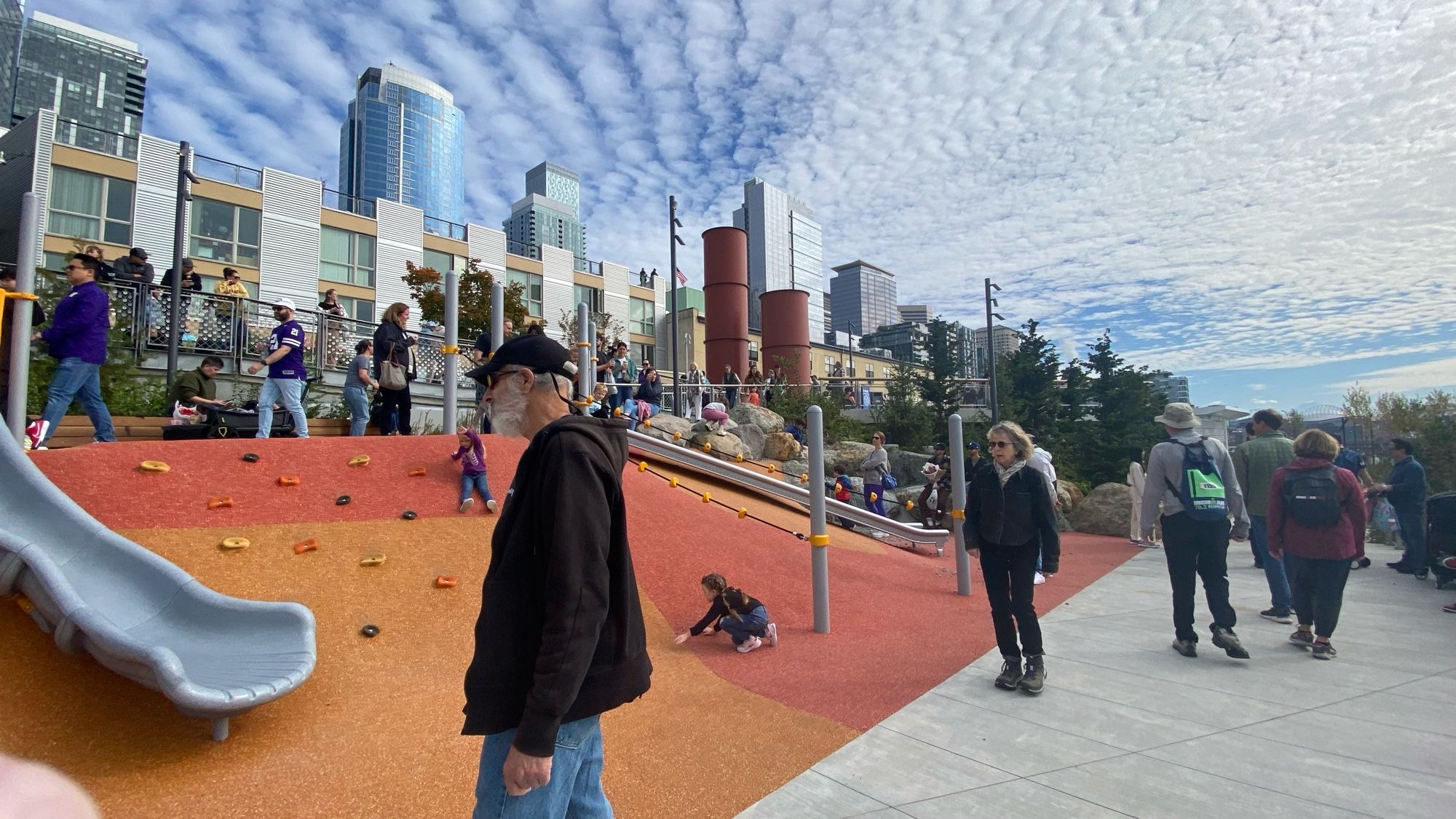 A playground for children links two different heights of pedestrian walkway and ramps. Slides skim the slope, and kids can climb back up using rock climbing handholds, or using ropes.