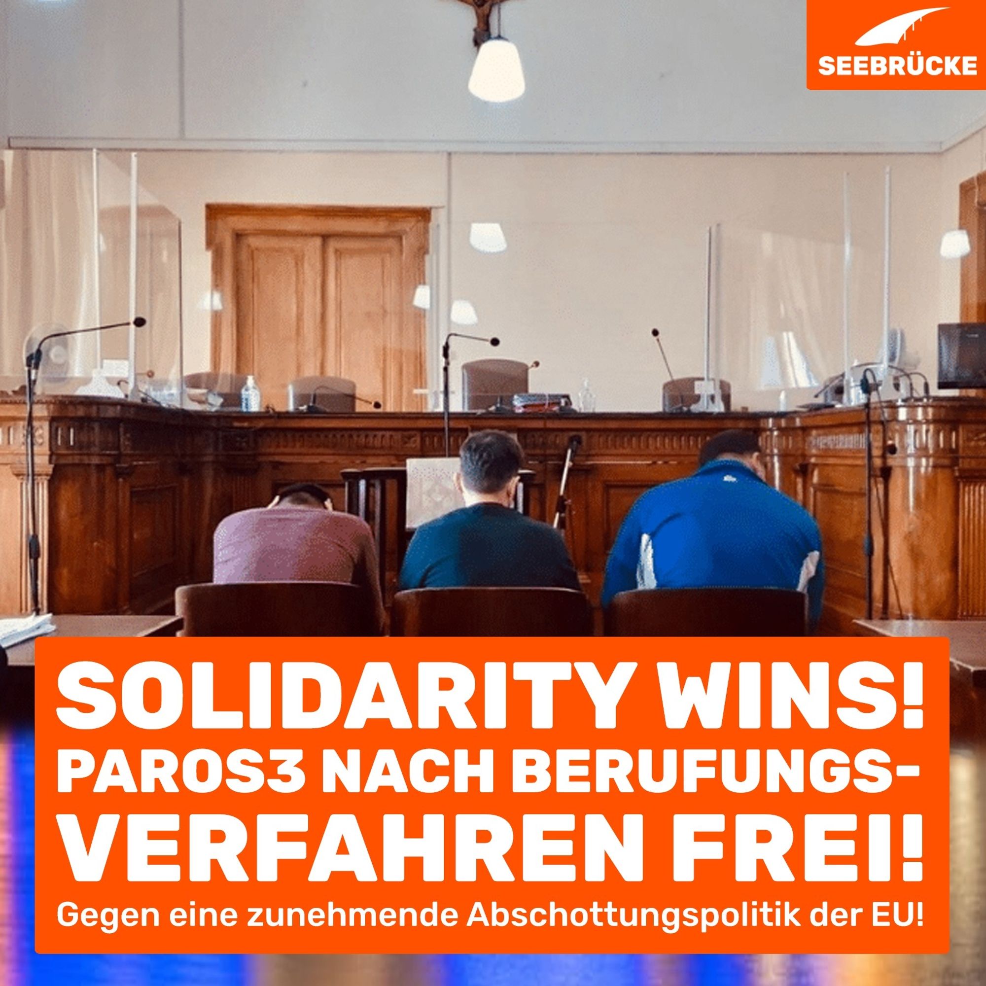 Photo of three men from behind in a courtroom. An orange box reads ‘Solidarity Wins! Paros3 free after appeal! Against the EU's increasing policy of sealing off borders!’. In the top right-hand corner is the Seebrücke logo in white on orange.