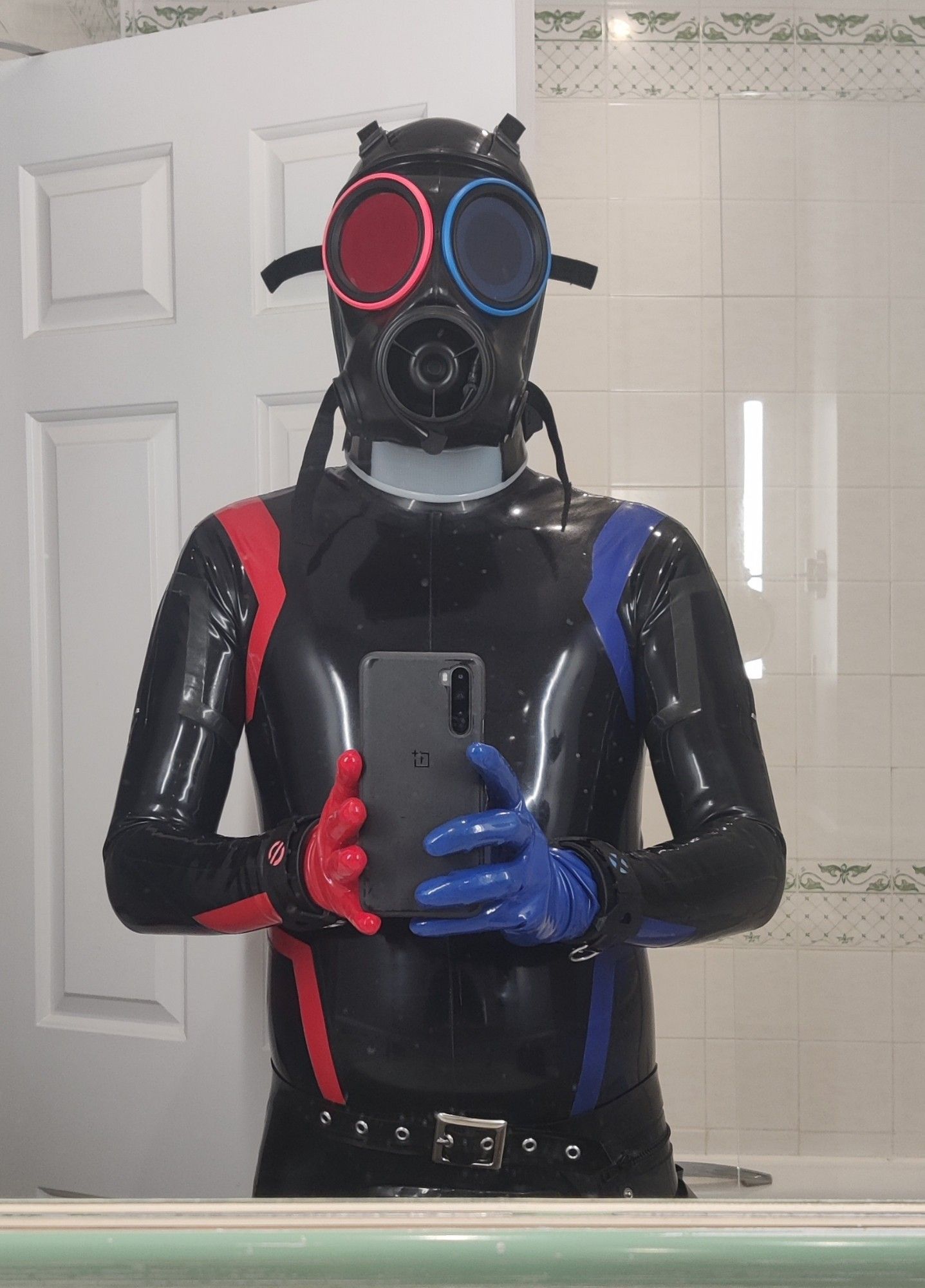 Upper body shot of a full latex drone in black blue and red taken in a hotel room bathroom