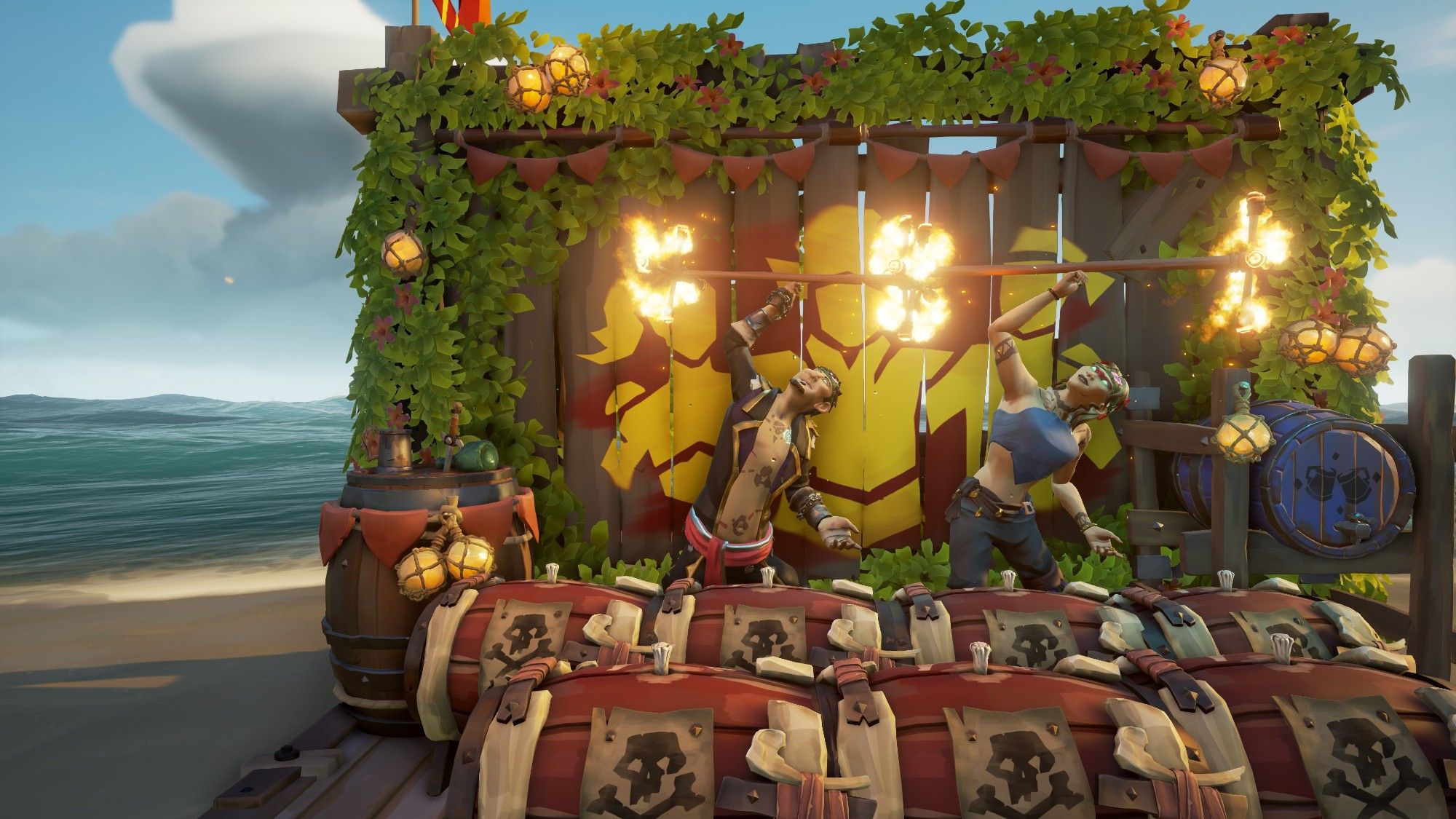 Two pirates in the video game Sea of Thieves holding torches on poles stand in front of the Community Day Photo Wall while standing in front of several Stronghold Kegs.