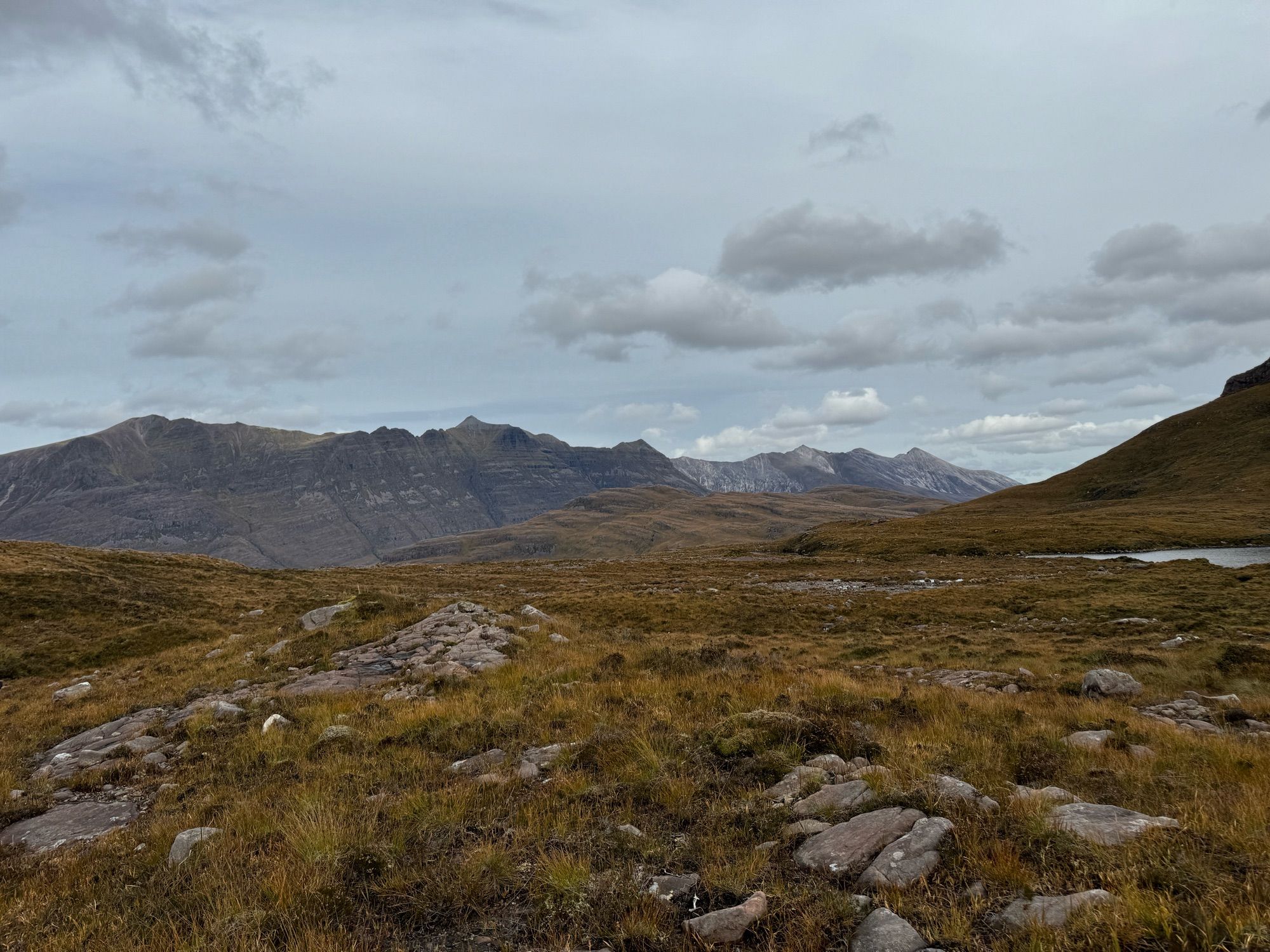 Scottish highlands. Two Munro’s in the background, Liathach and Beinn Eighe, with sharp ridge lines stretching away into the distance. In the foreground is a rock, grass and heather moorland.