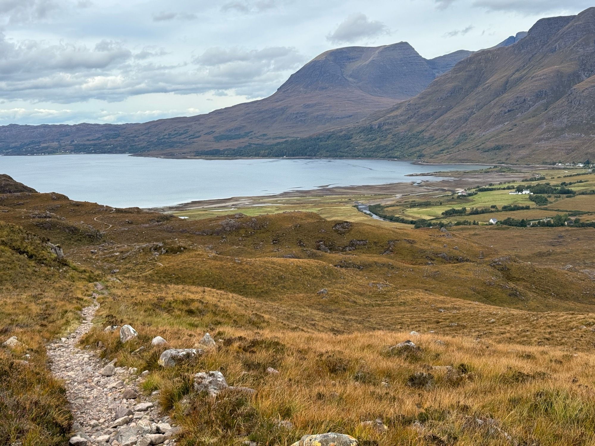 Scottish Highlands. Rough single track path weaving through grass & heather down to Loch Torridon. Two Munro’s, Beinn Alligin and Liathach, in the top right with Torridon village in the bottom right.