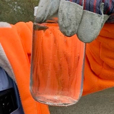 the same gloved hand holds the same style jar but it’s filled with clear cleaned water.