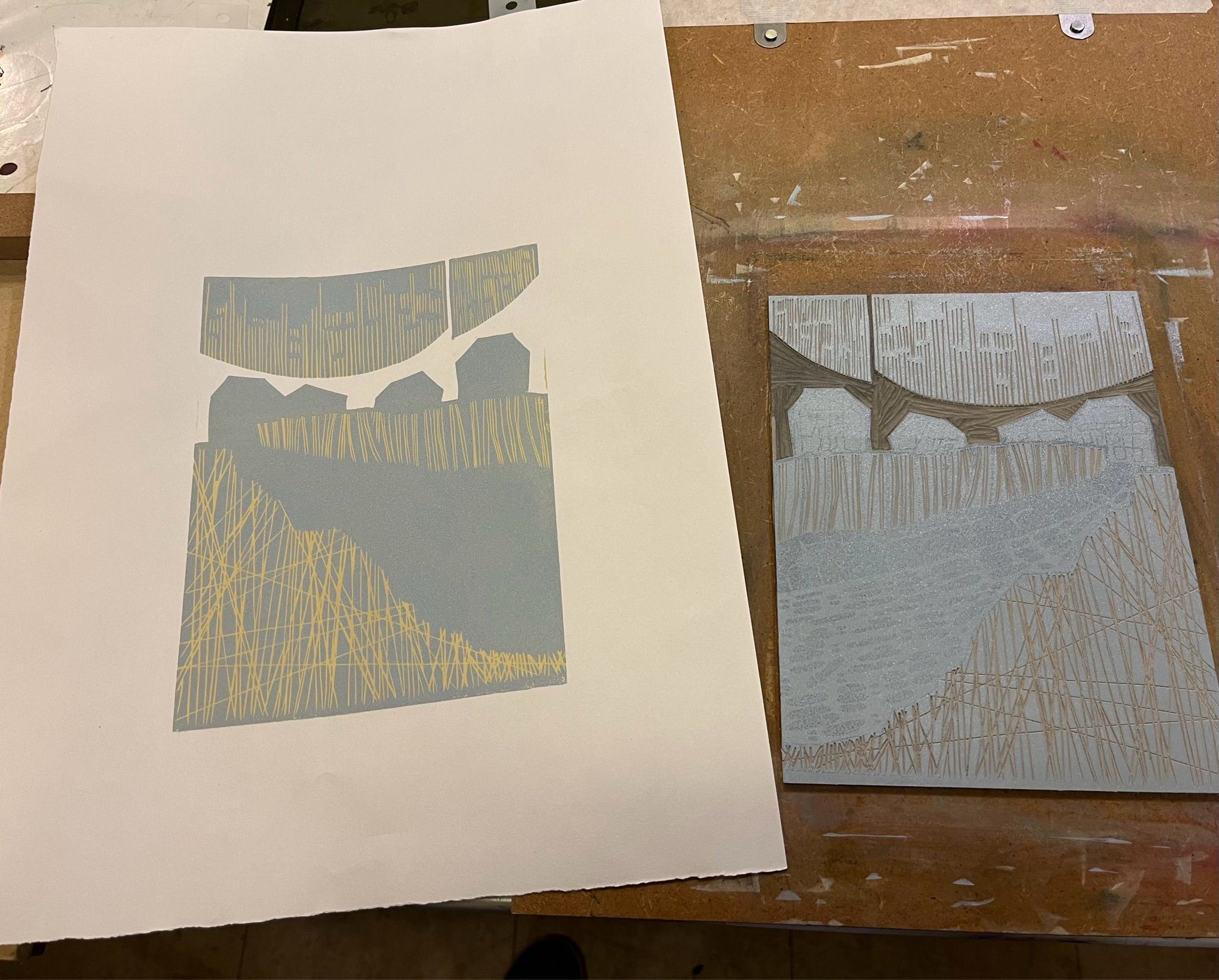 Photo of the lino block on its board with the second ink layer on the right, and the print on the left. One of the group described the colours (mid blue-grey over straw yellow) as mid-century modern so that’s what I’m going to use for inspiration for the rest of the ink layers.