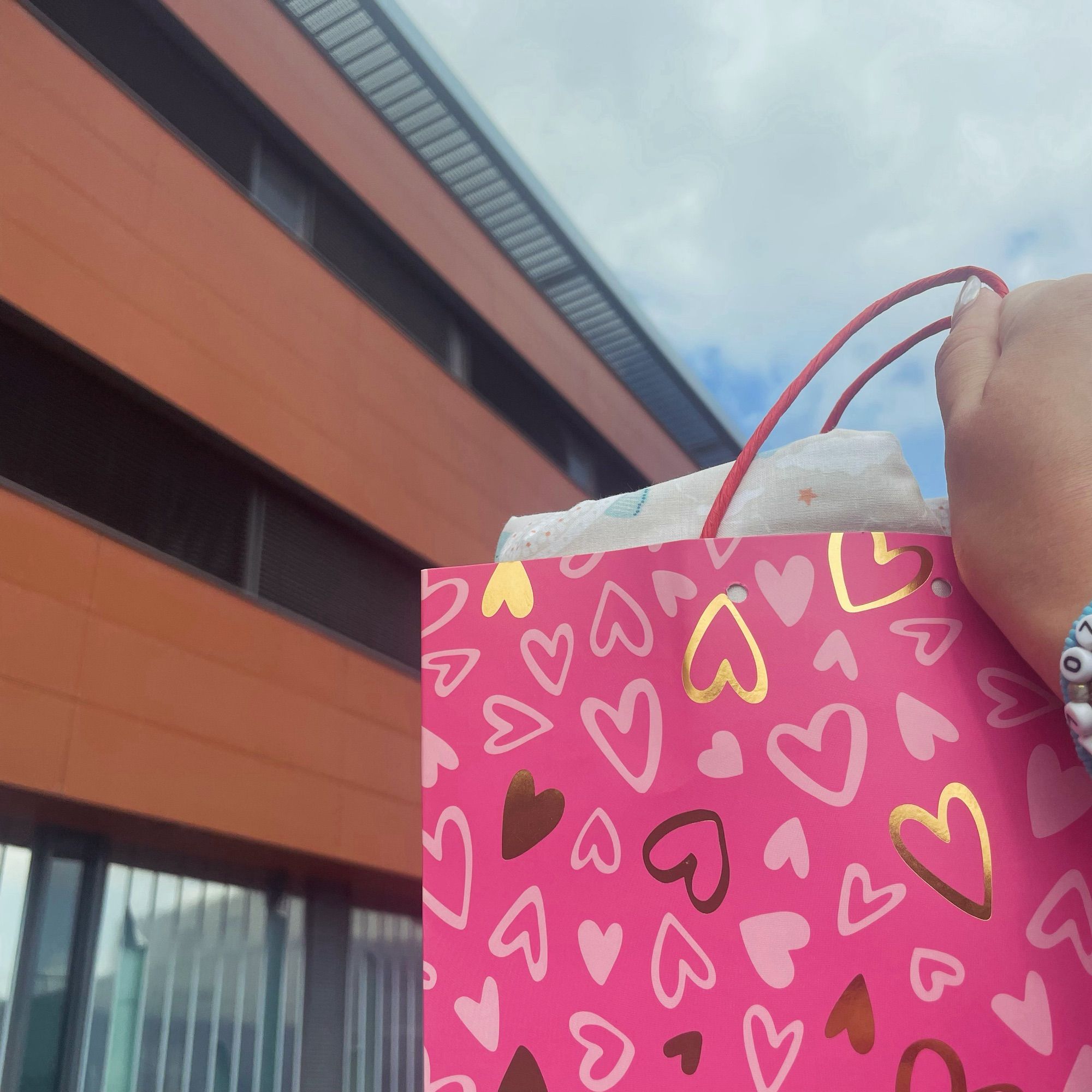 Sac cadeau rose avec des motifs cœurs dans lequel on devine une couverture devant un hôpital marron