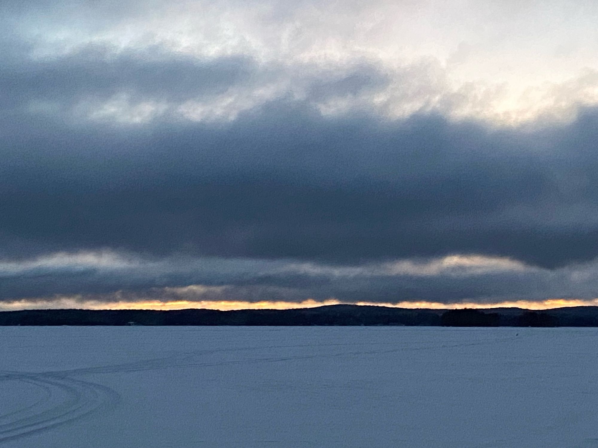 Järvellä ennen auringon nousua on musteensinisiä pilviä. Taivaanrannasta loistaa keltainen viiru.