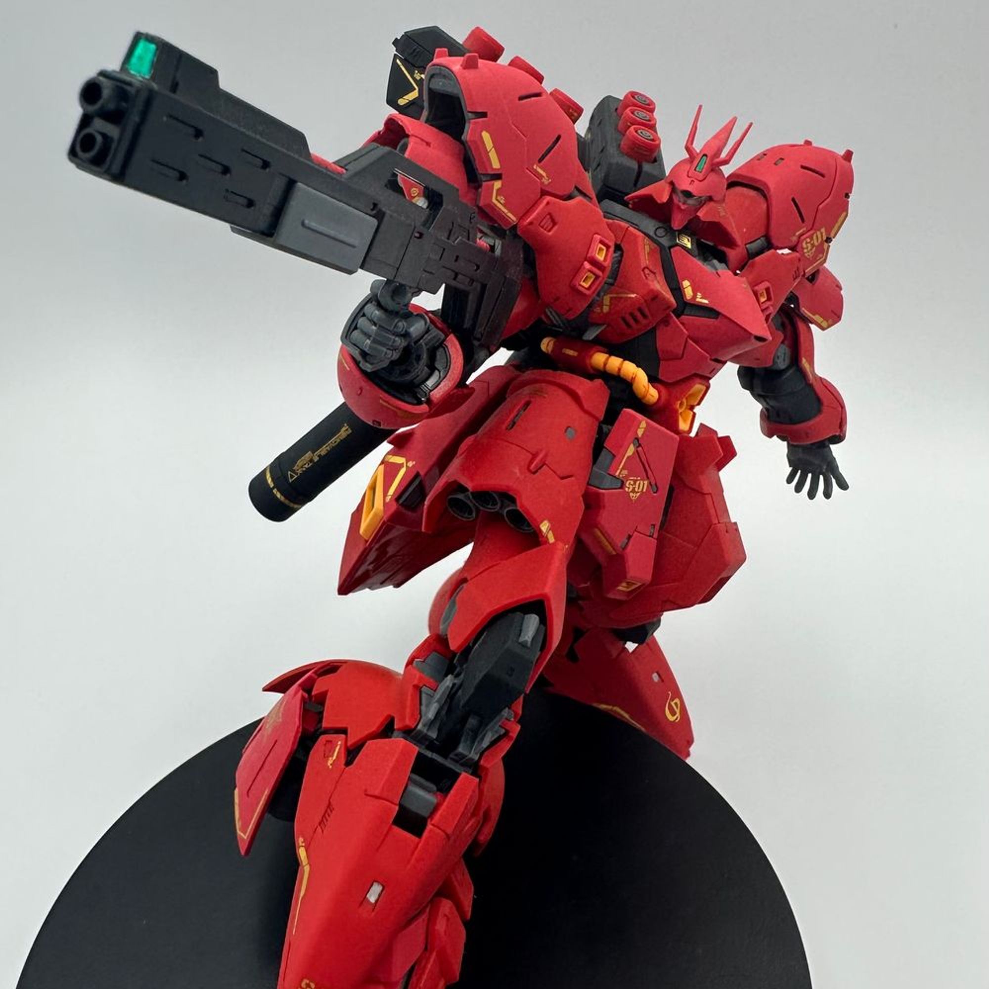 A photo of the 1/144 RG Sazabi Gundam. It is holding an action pose with a foot on a small stand. 