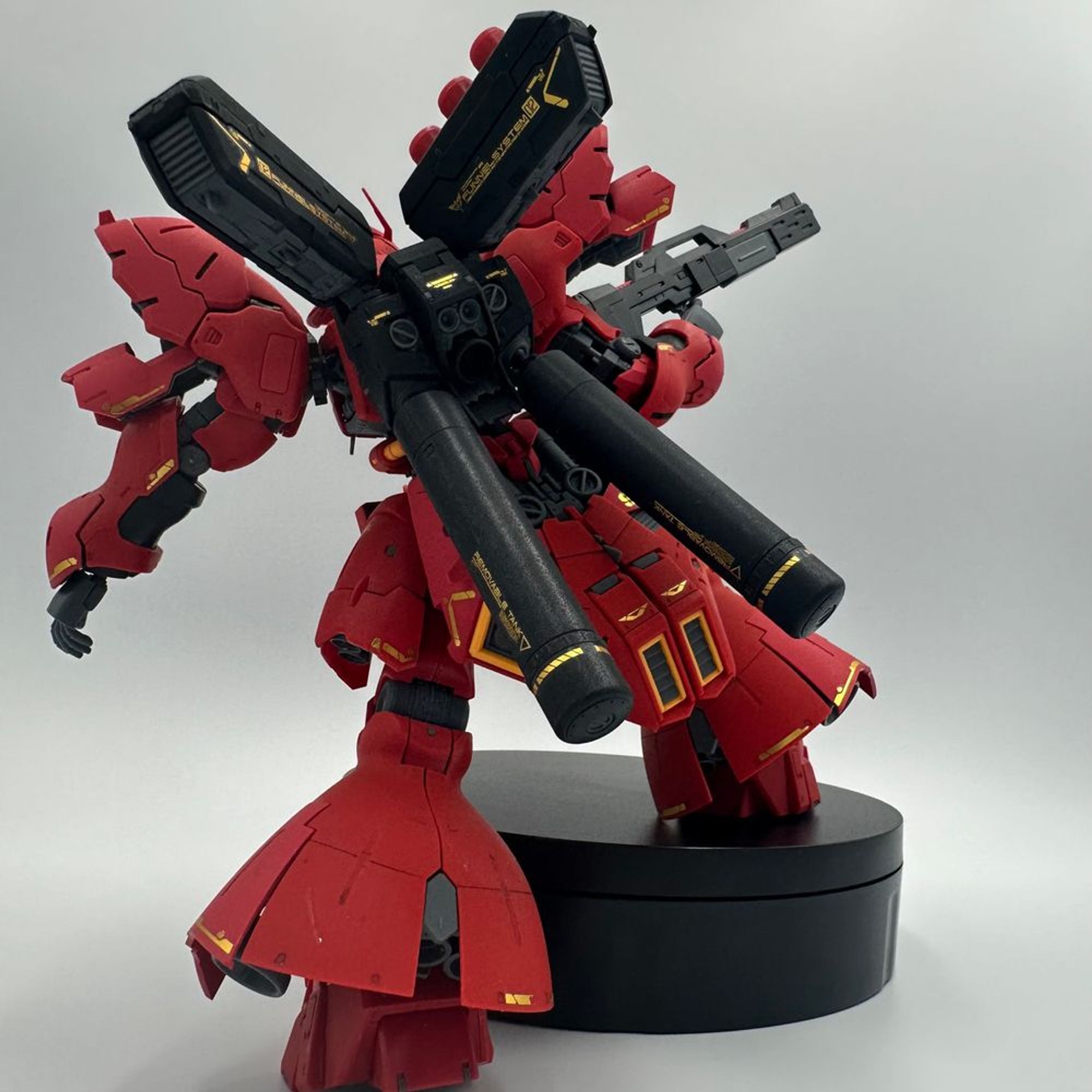 A photo of the back of the 1/144 RG Sazabi Gundam. It is holding an action pose with a foot on a small stand. 