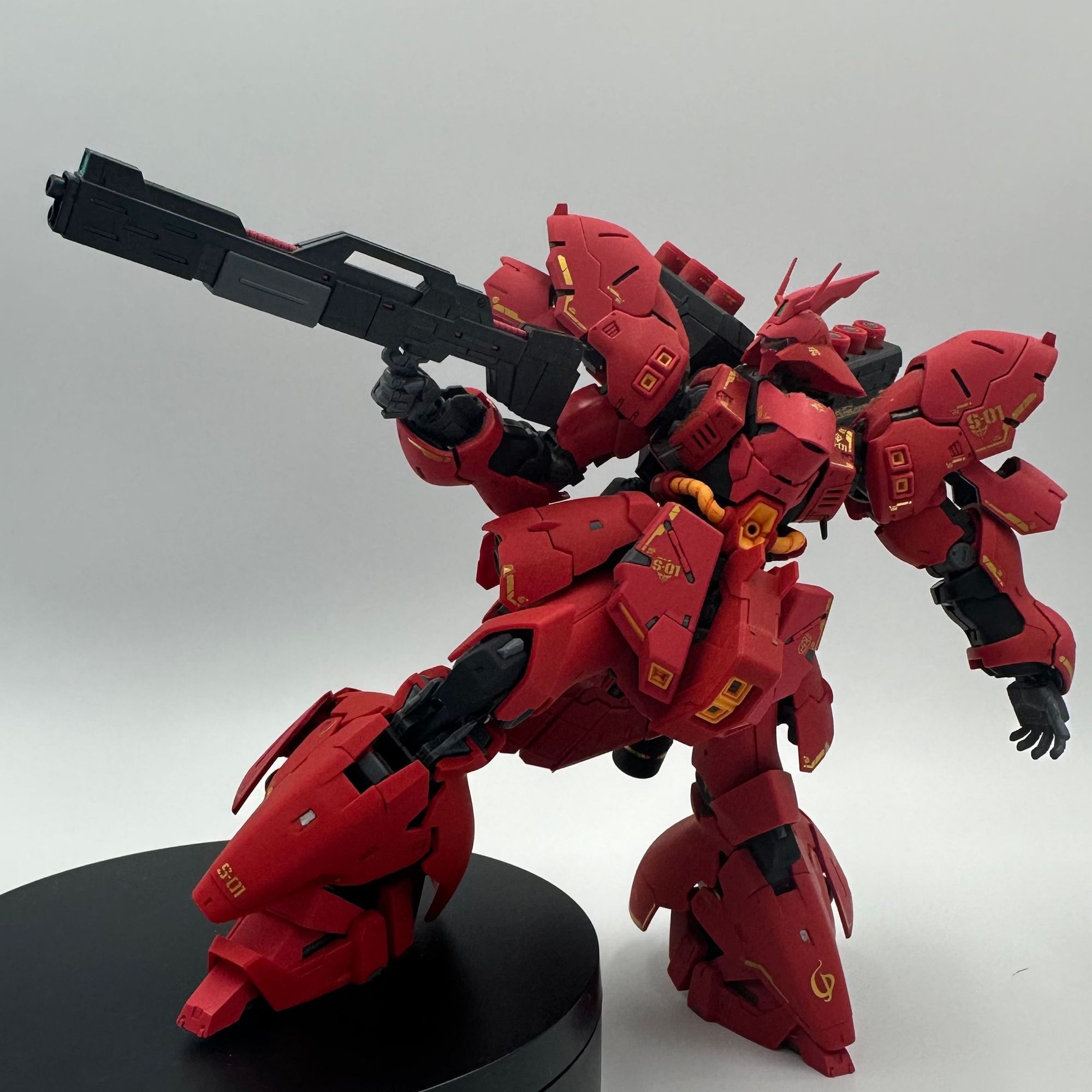 A photo of the 1/144 RG Sazabi Gundam. It is holding an action pose with a foot on a small stand. 